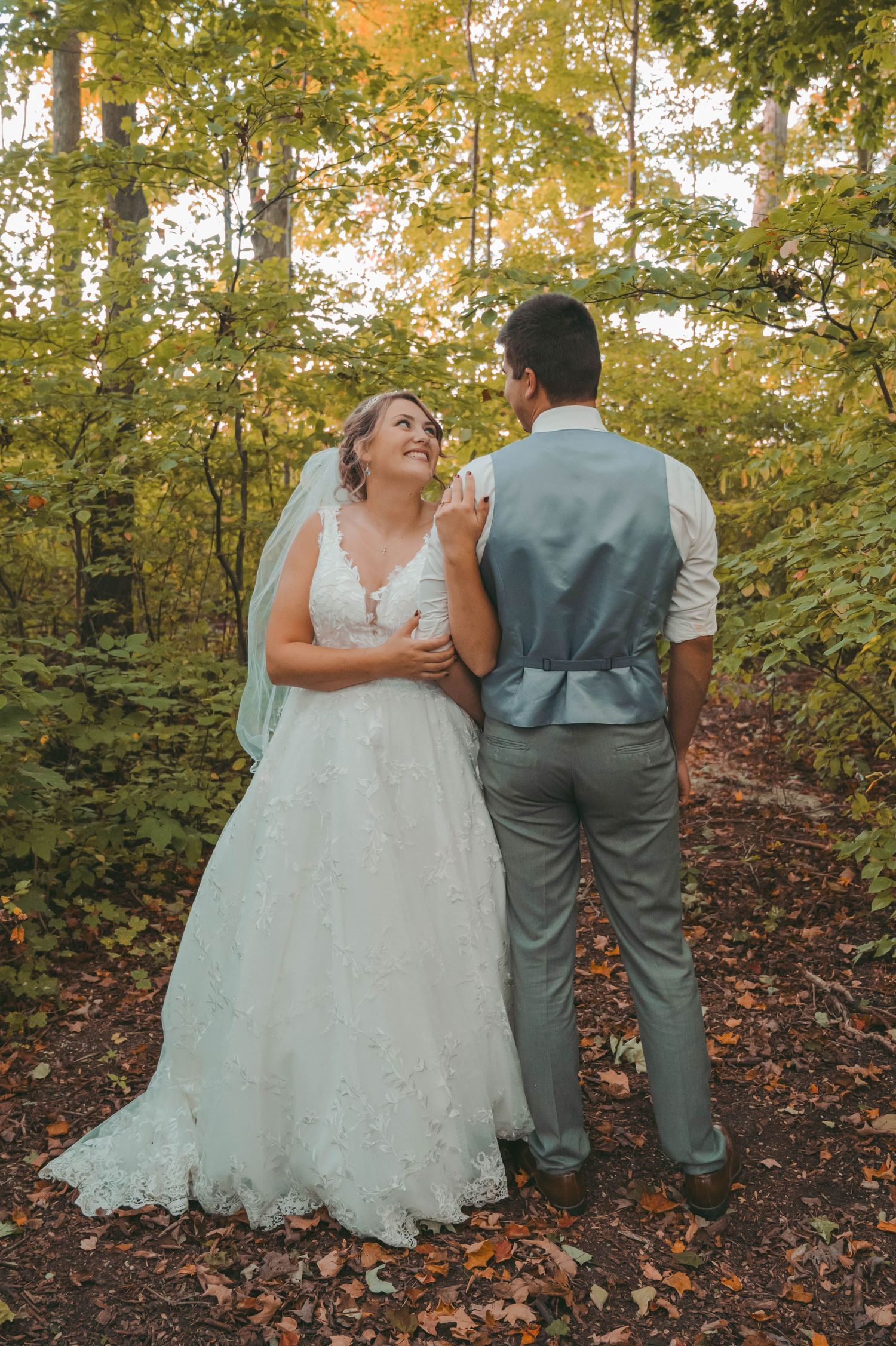 A wedding couple shares a joyful moment in a fall forest setting with golden leaves in the background.