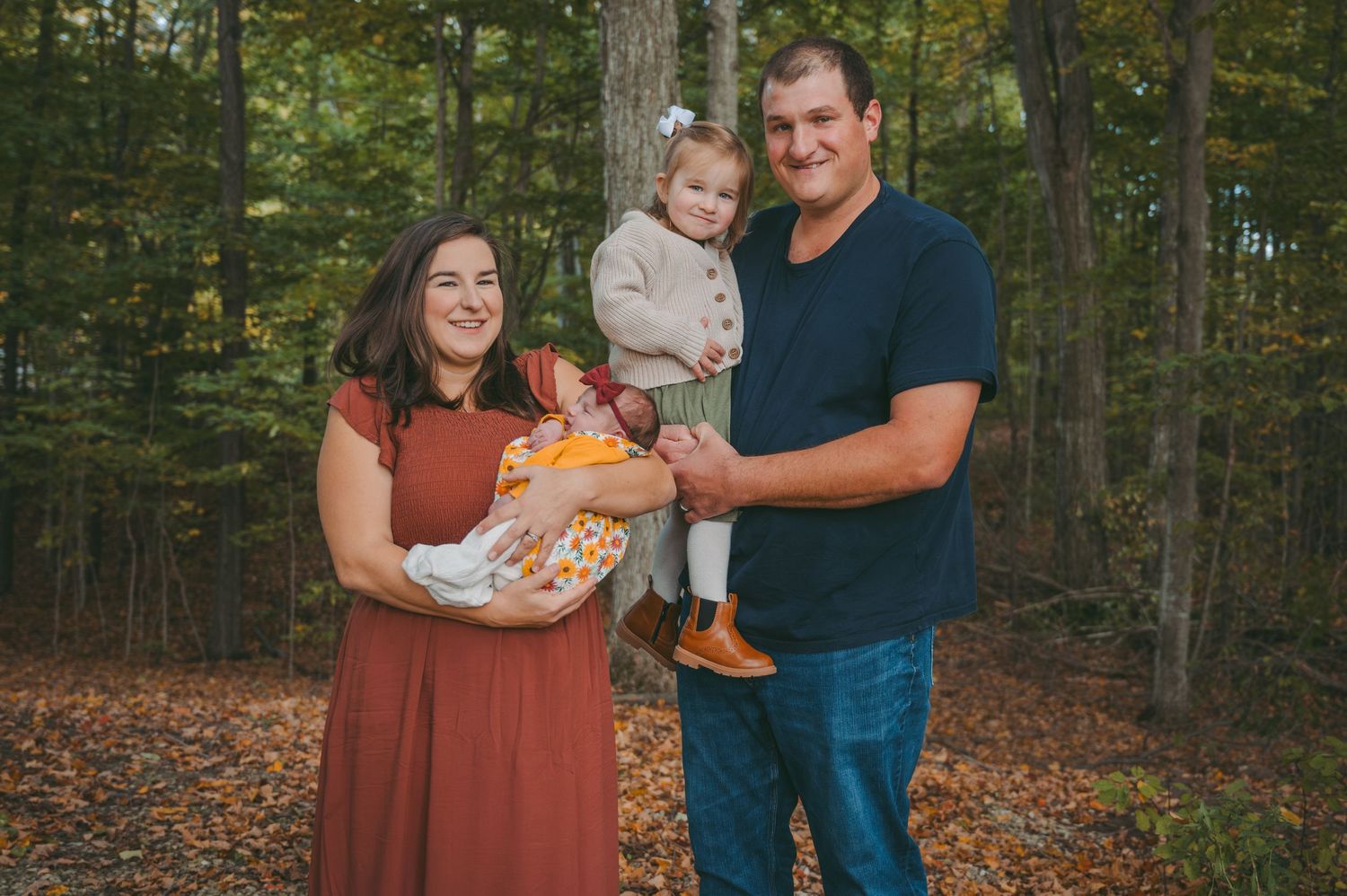 Family portraits taken in a wooded setting during autumn with warm earth-toned clothing.