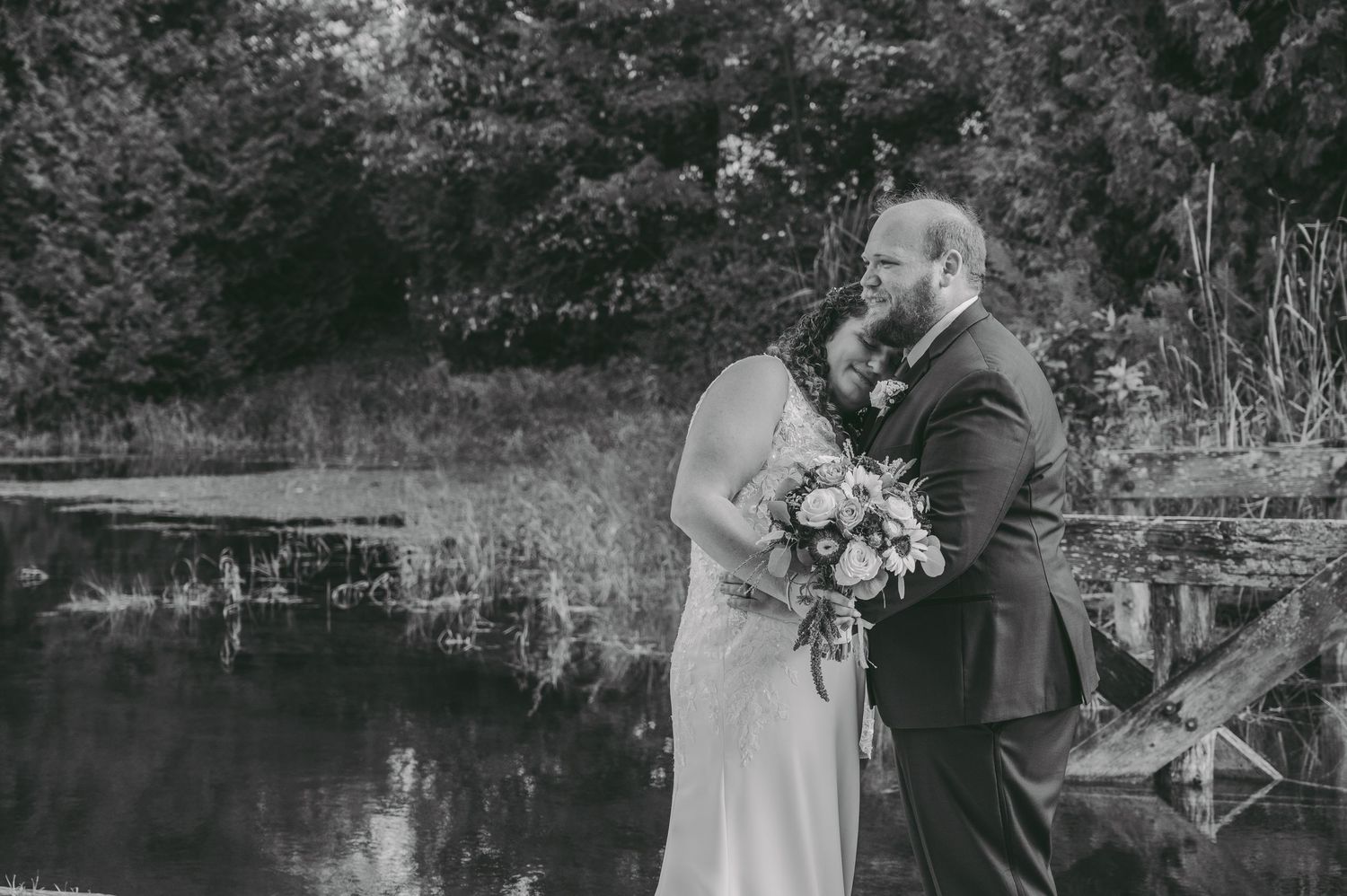 A black and white portrait of a couple sharing an intimate moment by a serene pond.
