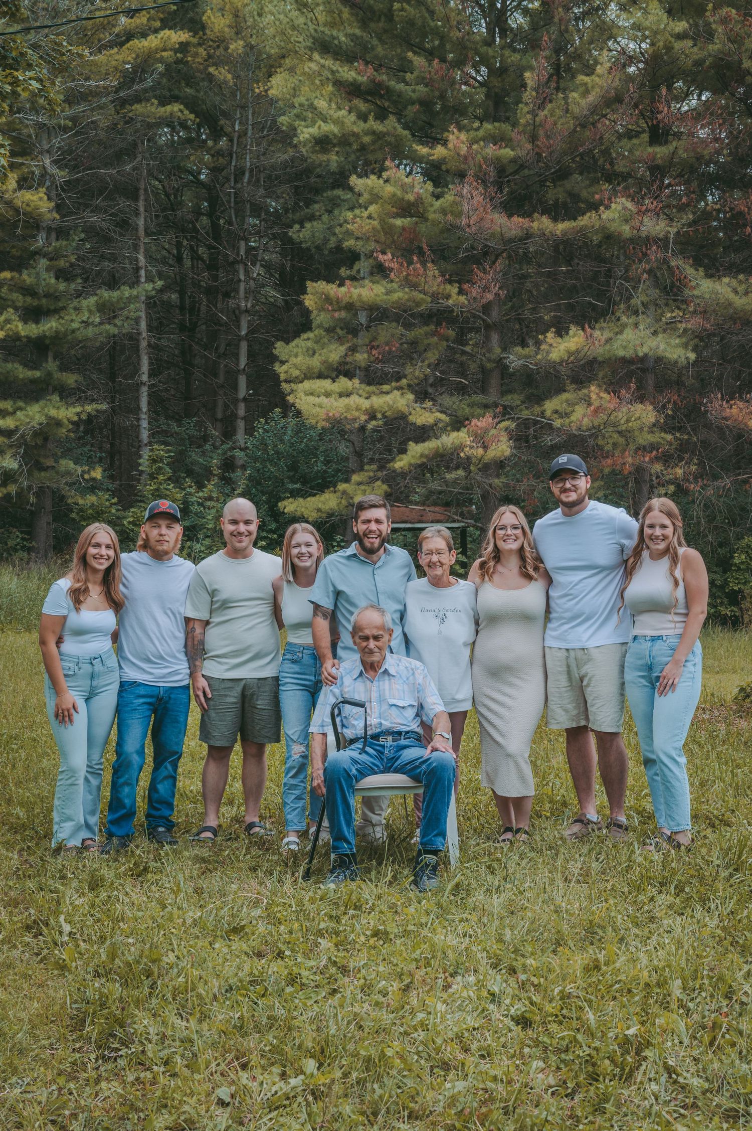 Extended family group poses together outdoors against a backdrop of evergreen trees.