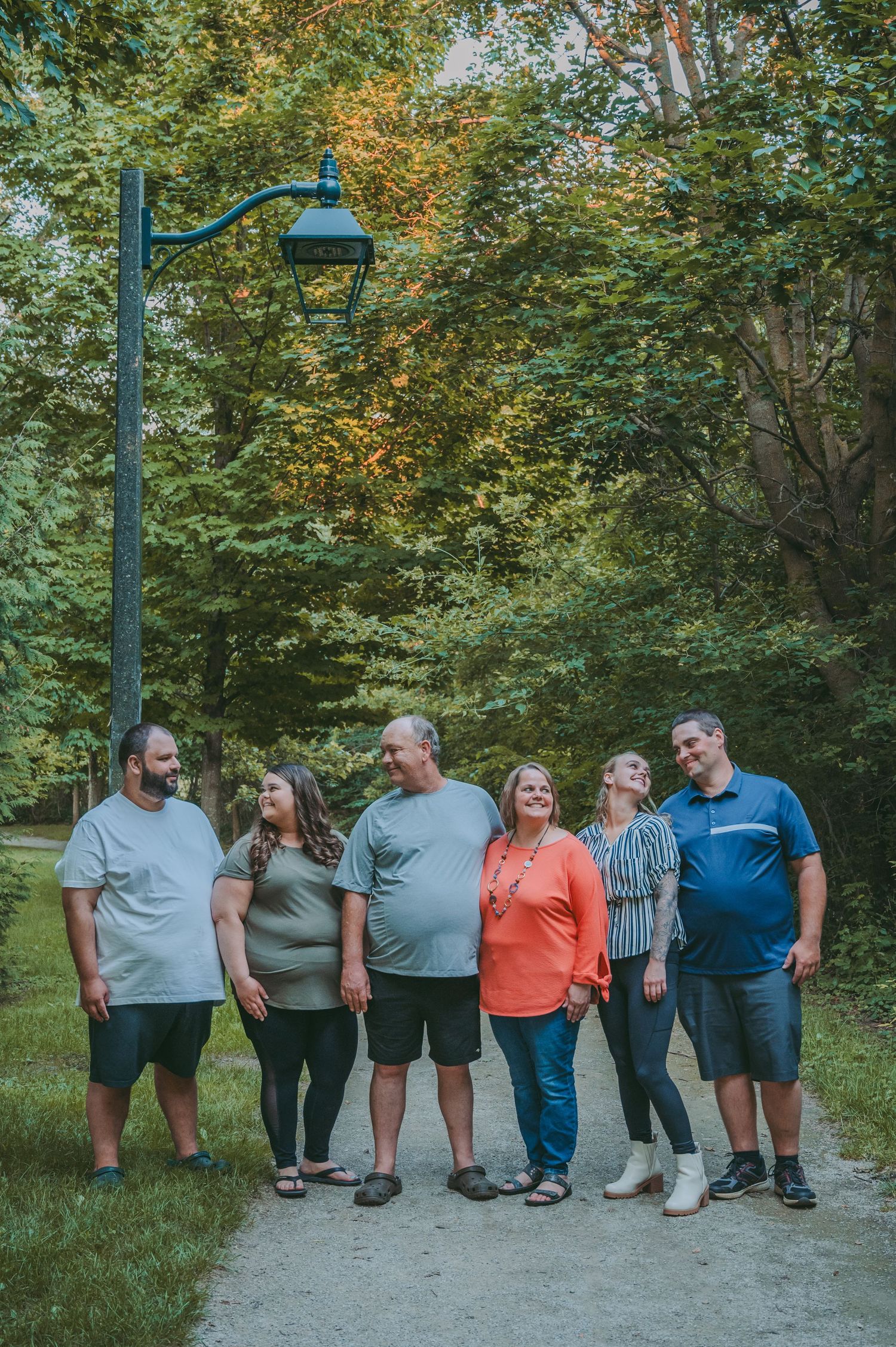 Group photo session on a path surrounded by lush green trees in a park setting.