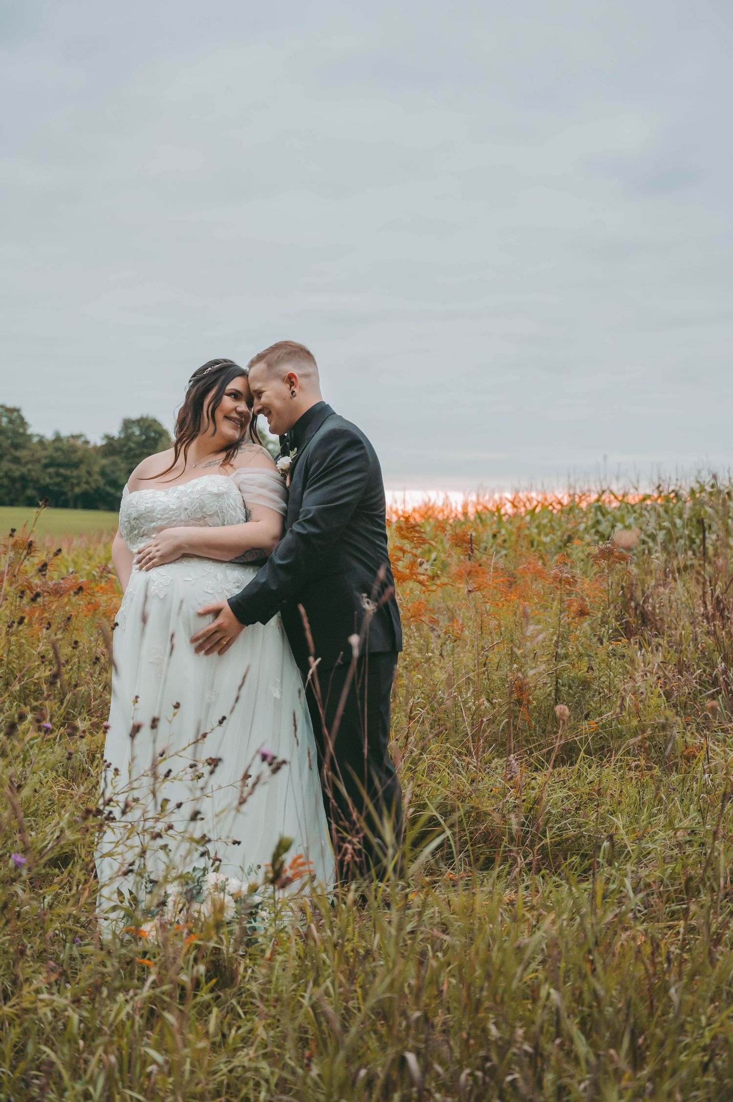 A tender embrace between newlyweds in a golden field at sunset.