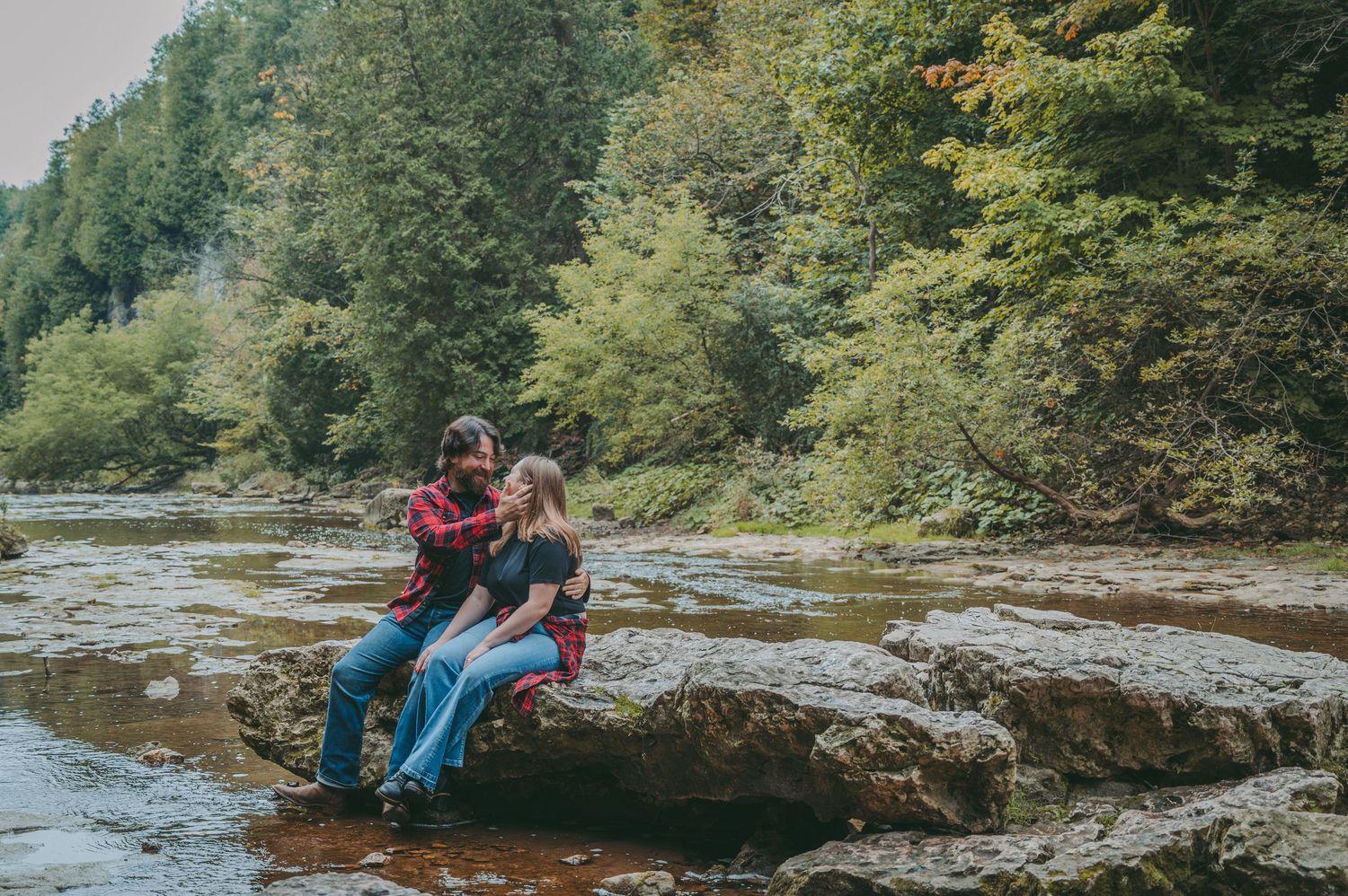 Rocky riverbed surrounded by dense forest during fall season with natural lighting.