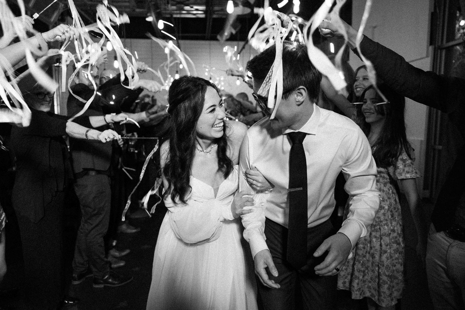 Black and white photo of dancing couple surrounded by ribbon wands at wedding reception.