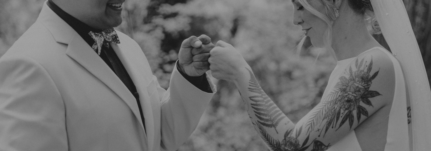 Black and white photo showing a couple exchanging rings during an outdoor wedding ceremony.