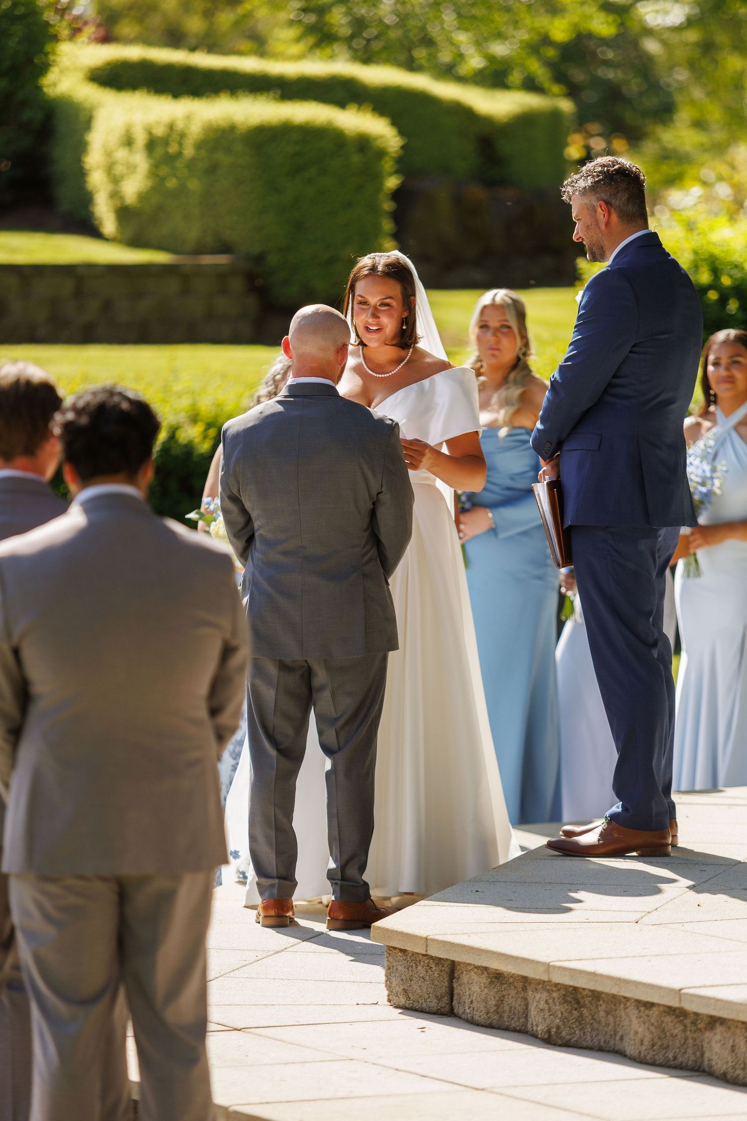 Wedding party gathered outdoors on sunny stone patio in blue and white attire.