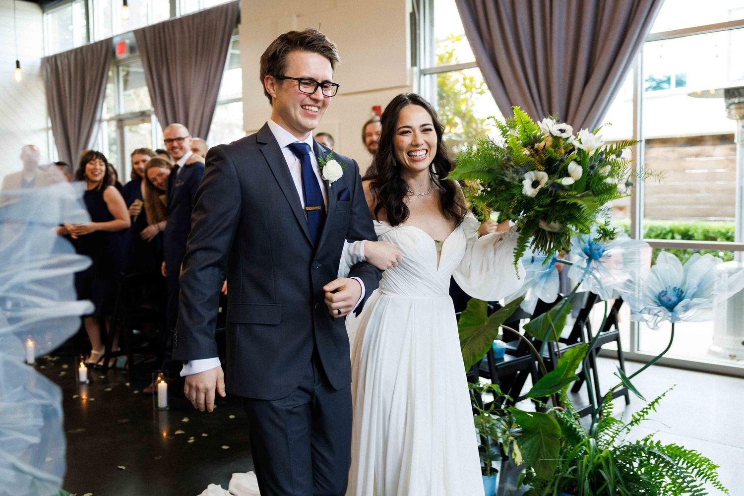 Joyful wedding recessional with couple walking down aisle amid greenery and flowers.