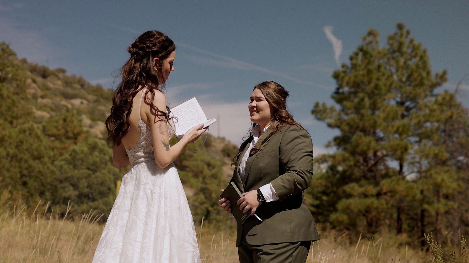 Two brides embracing in flower garden surrounded by trees in Flagstaff, Arizona | LGBTQ+ mountain wedding at Viola’s Flower Garden