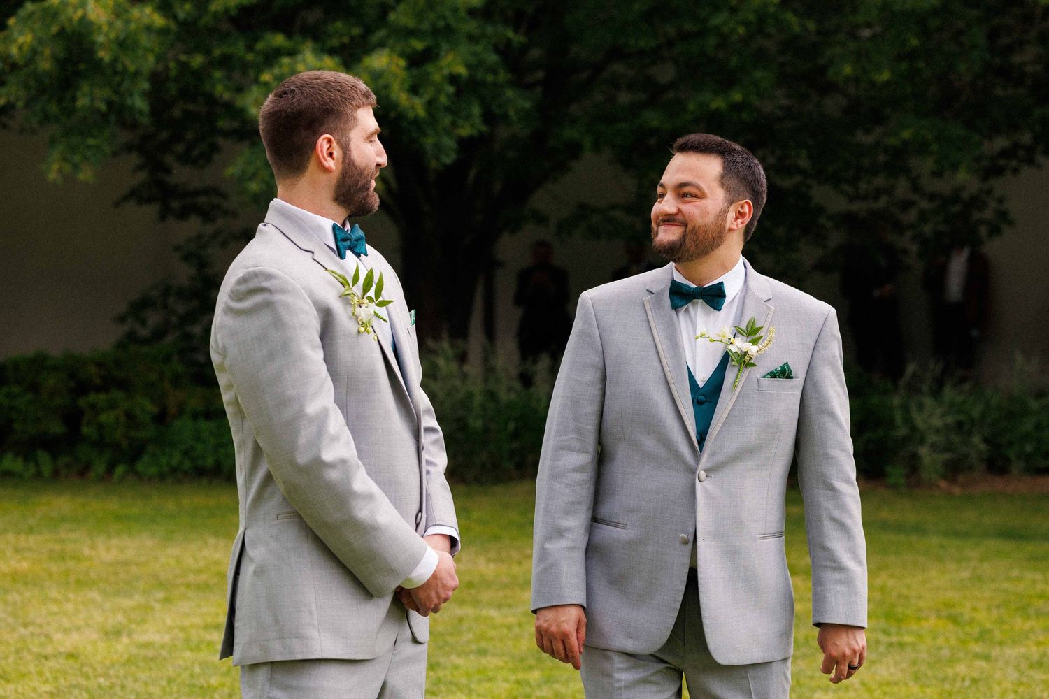 Two grooms in matching gray suits sharing a happy moment outdoors.