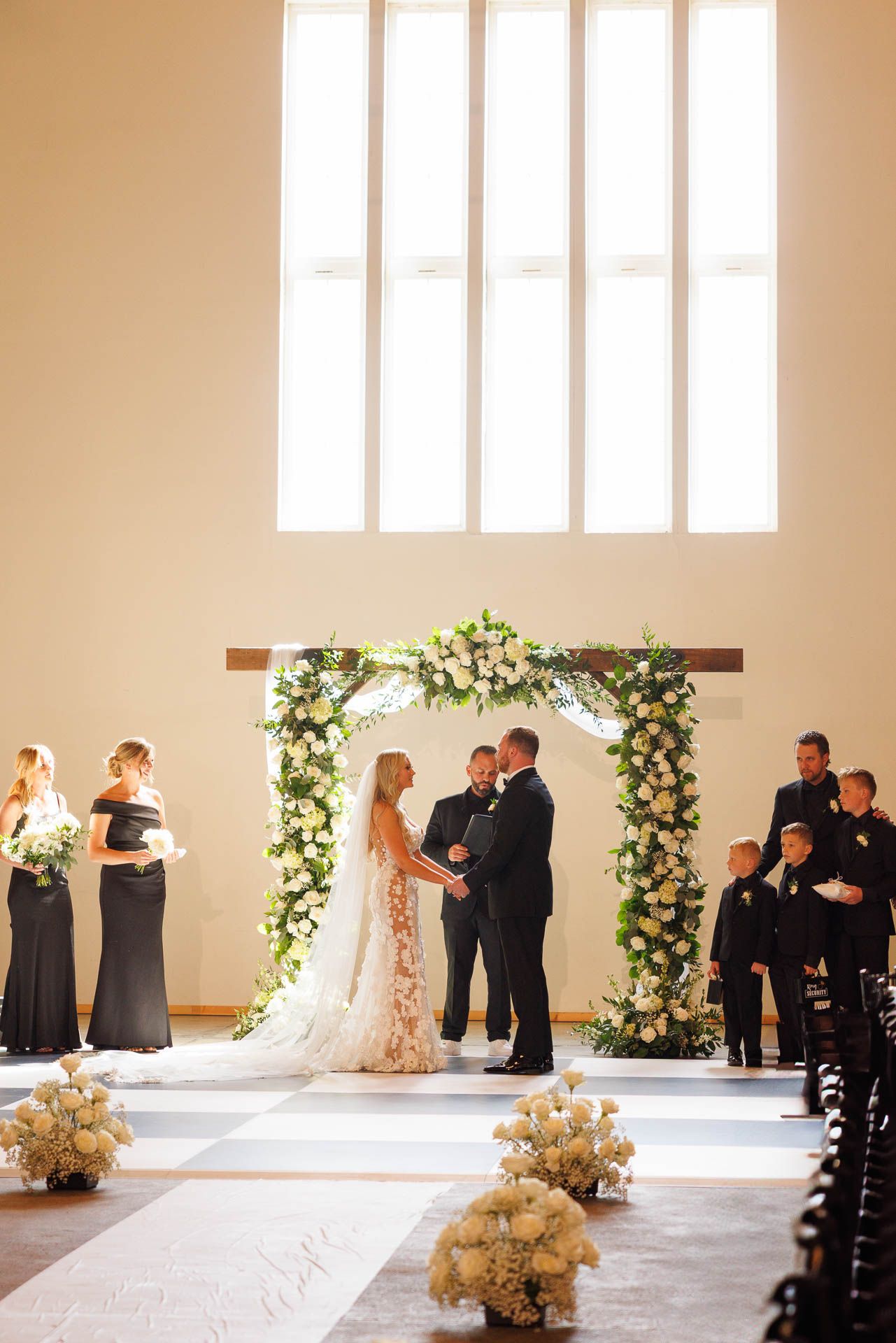 An elegant wedding ceremony under a floral arch in a bright minimalist indoor venue.