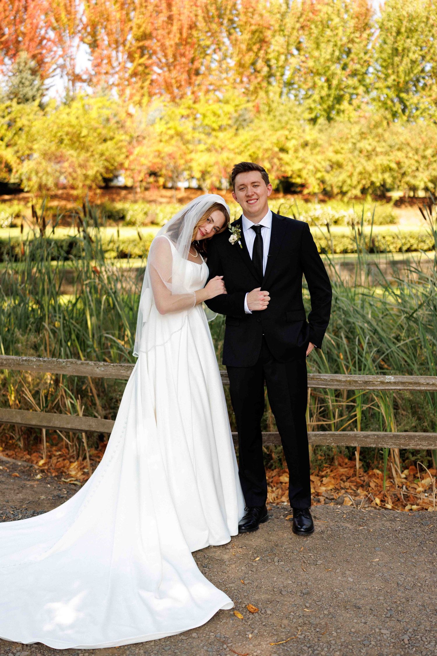 Newlyweds embracing on walkway with beautiful fall foliage in background.