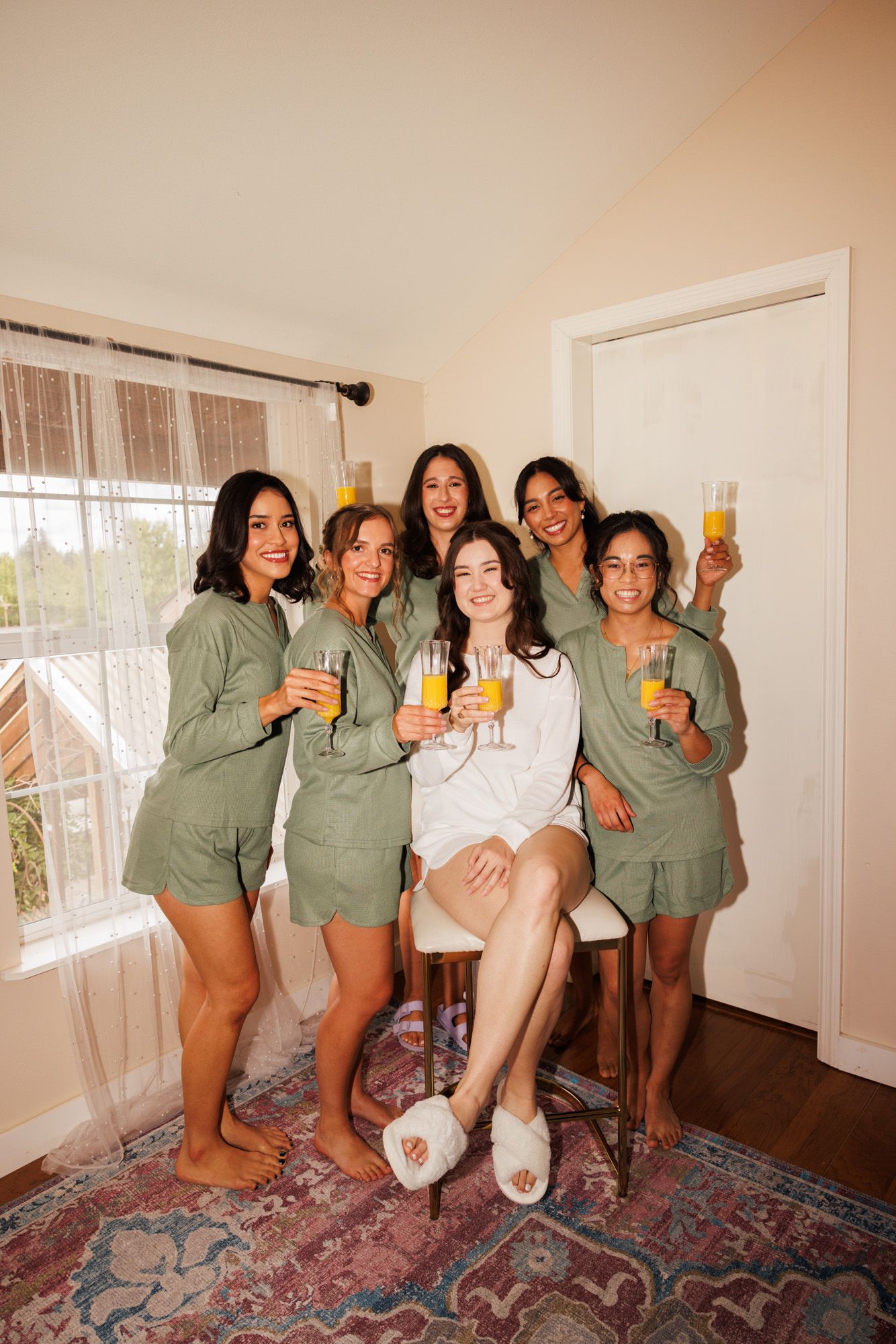 A group wearing matching sage green loungewear poses together while holding mimosas.