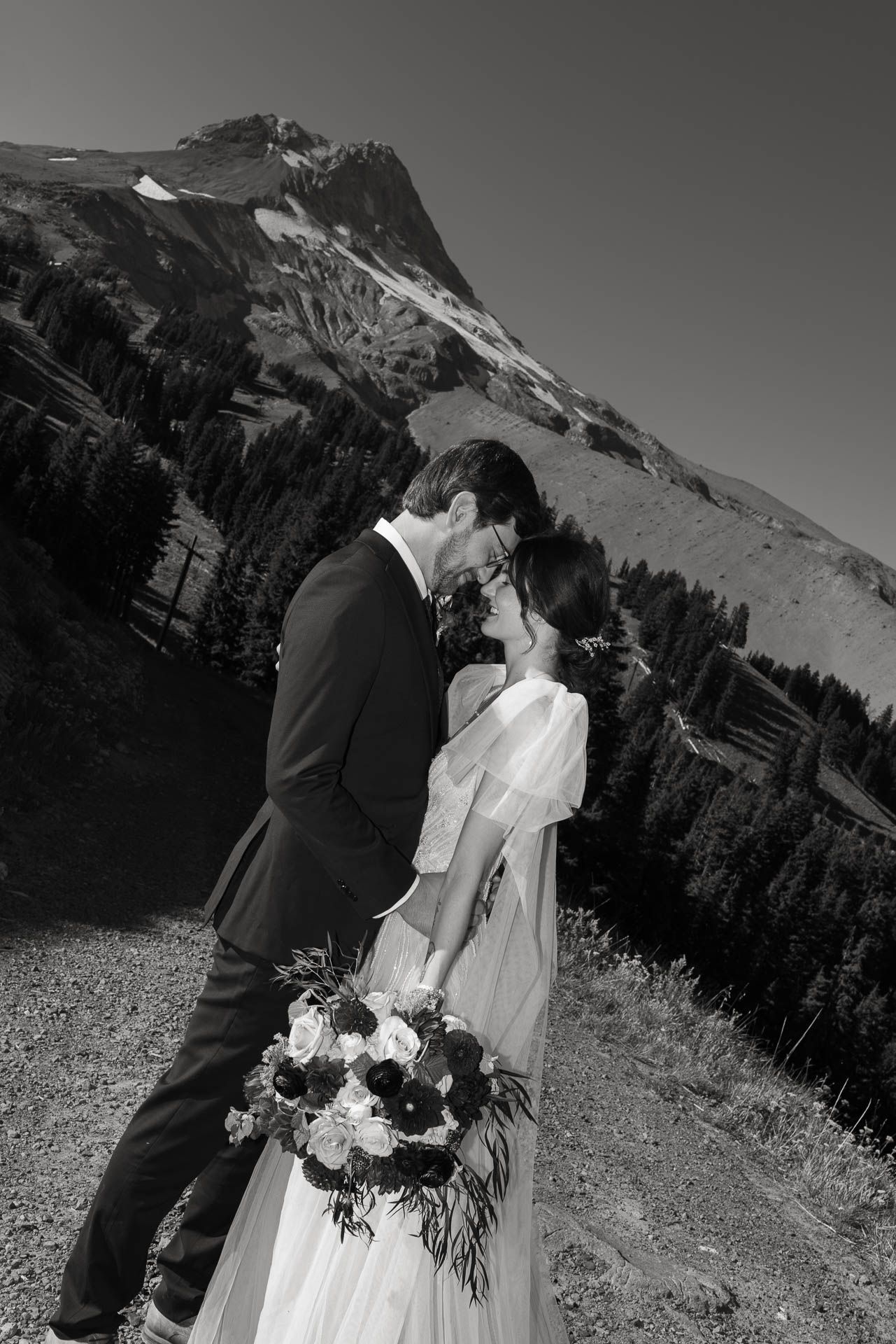 A romantic black and white wedding portrait with a dramatic mountain backdrop.