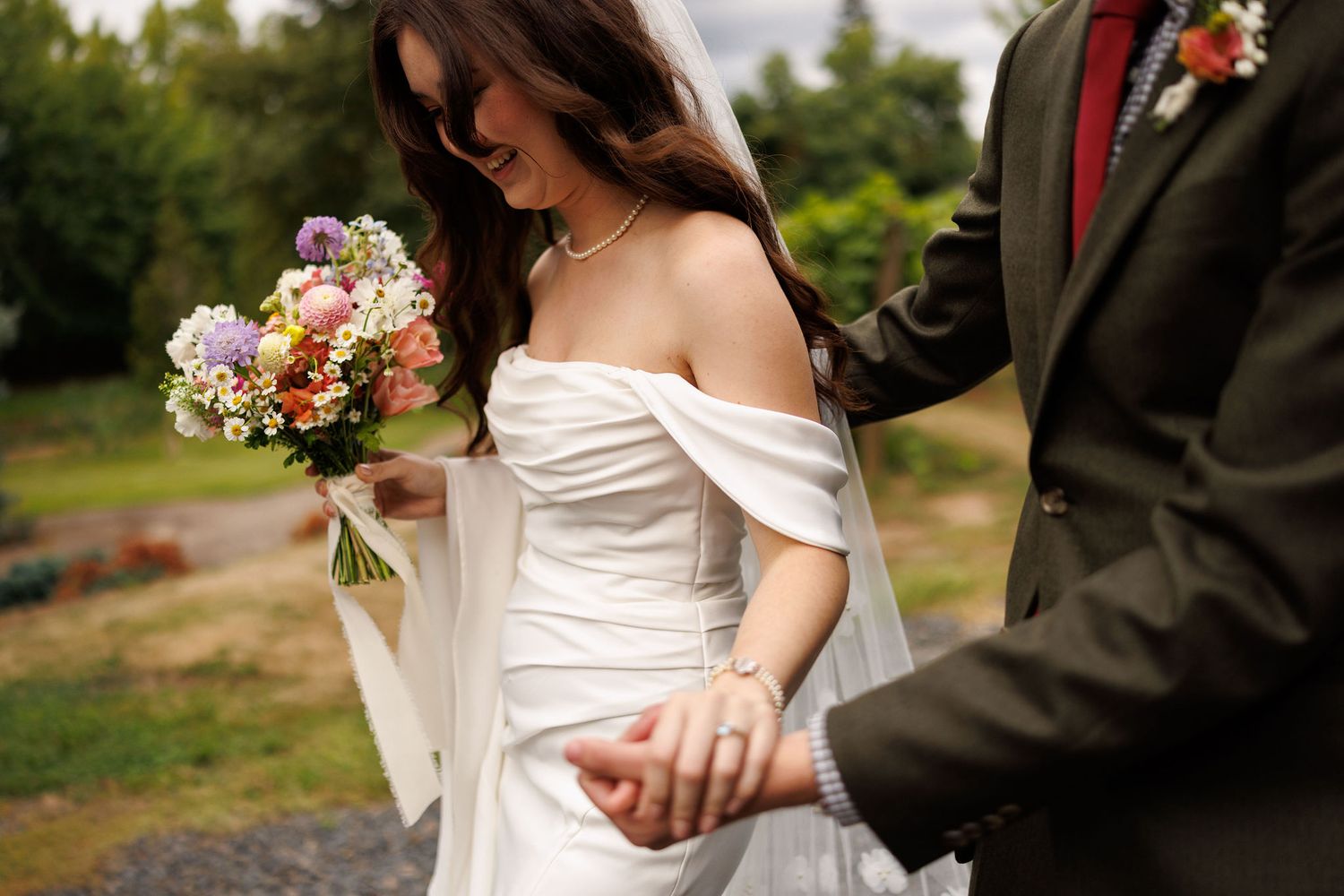 Close-up shot of couple holding hands with peach and white wedding bouquet.