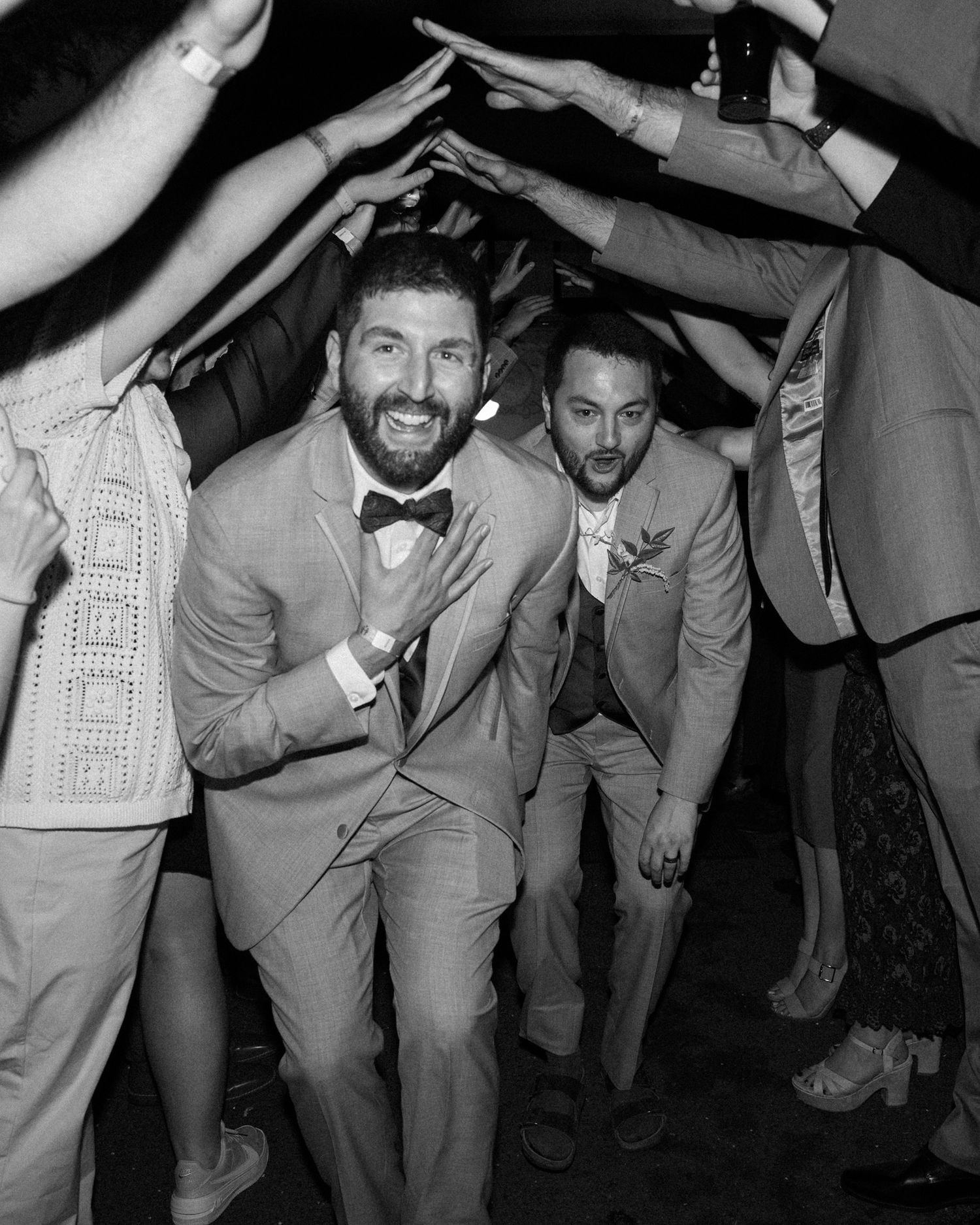 Joyful couple walking under an arch of raised arms during a wedding celebration reception.