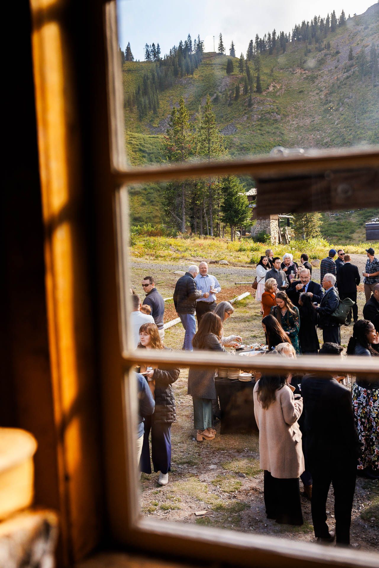 A wedding ceremony viewed through a window with mountain scenery in the background.