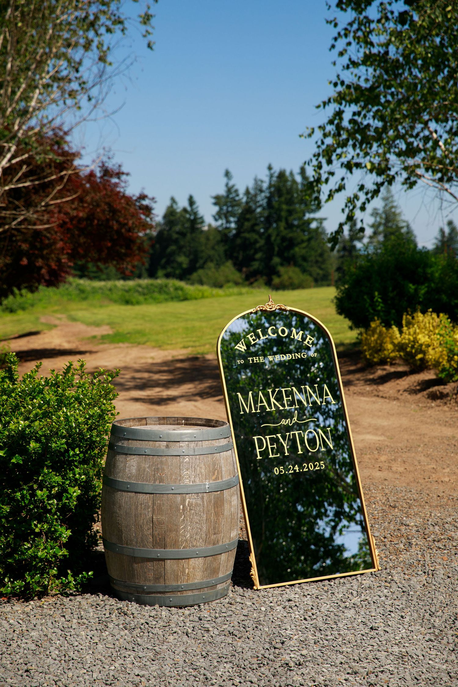 Rustic vineyard wedding decor with wine barrels and chalkboard signs on gravel path.