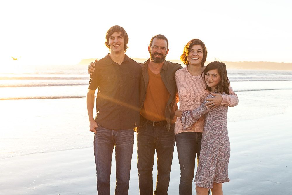 A playful family of four captured in a golden-hour hug on the beach. Natural, joyful portraits full of connection and love.