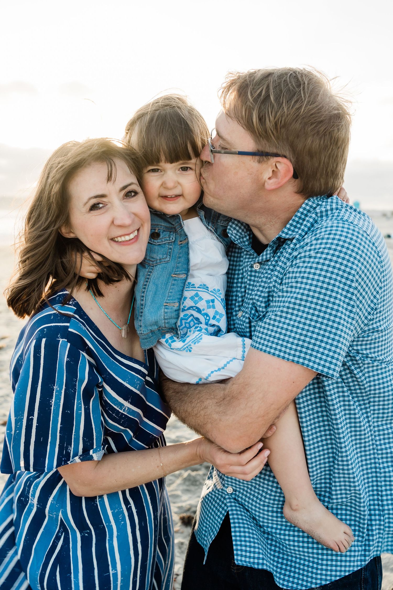 Mom and dad kissing their daughter’s cheeks during golden hour – joyful family portrait on Coronado Beach