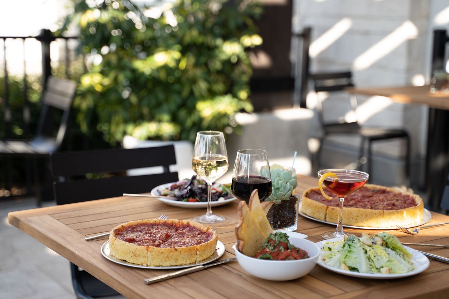 Outdoor pizzeria patio at dusk with twinkle lights, deep dish pizza, and shared salad – lifestyle food photography