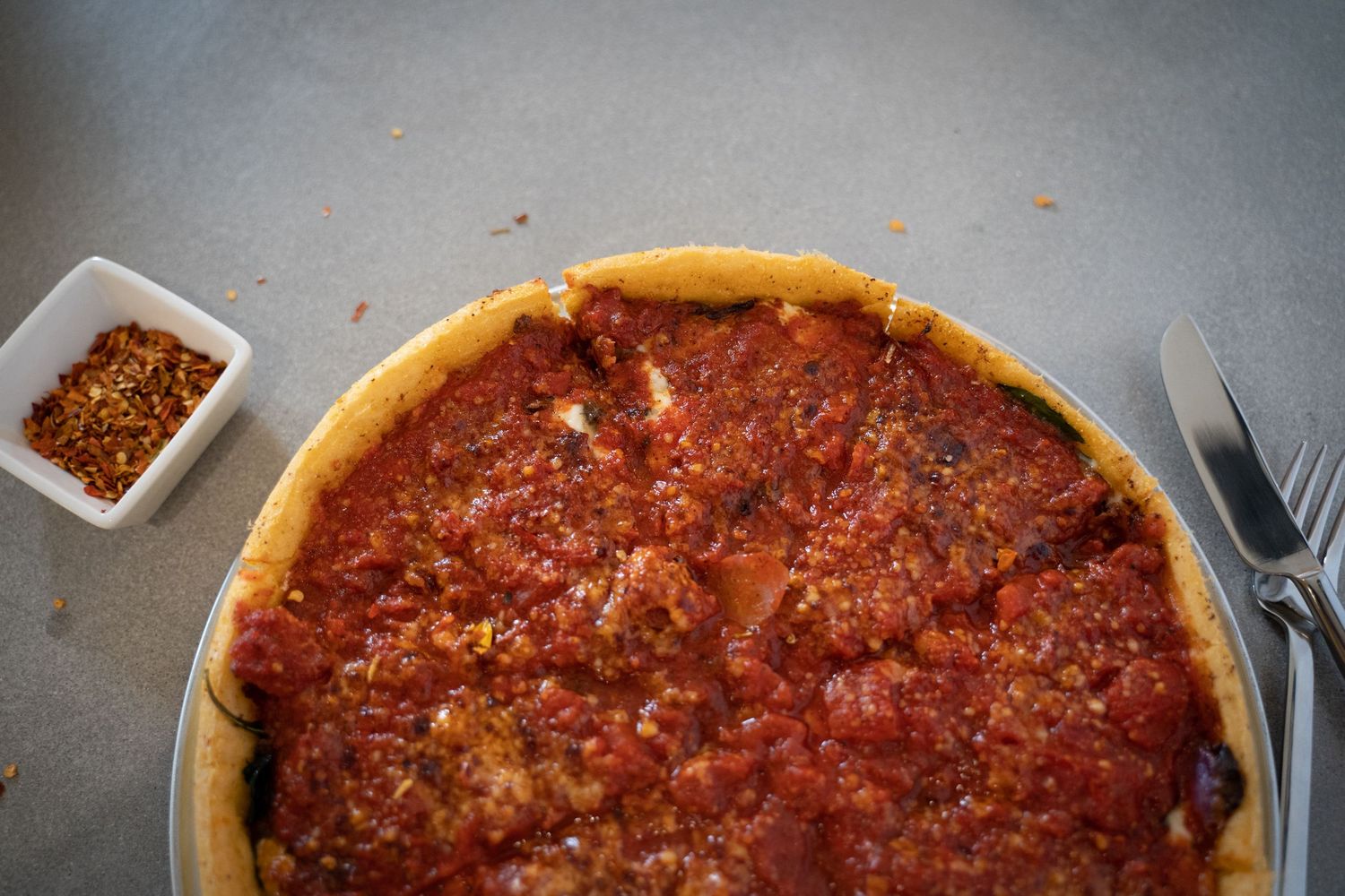 Thick-crust deep dish pizza with layers of cheese and tomato sauce in a cast iron pan