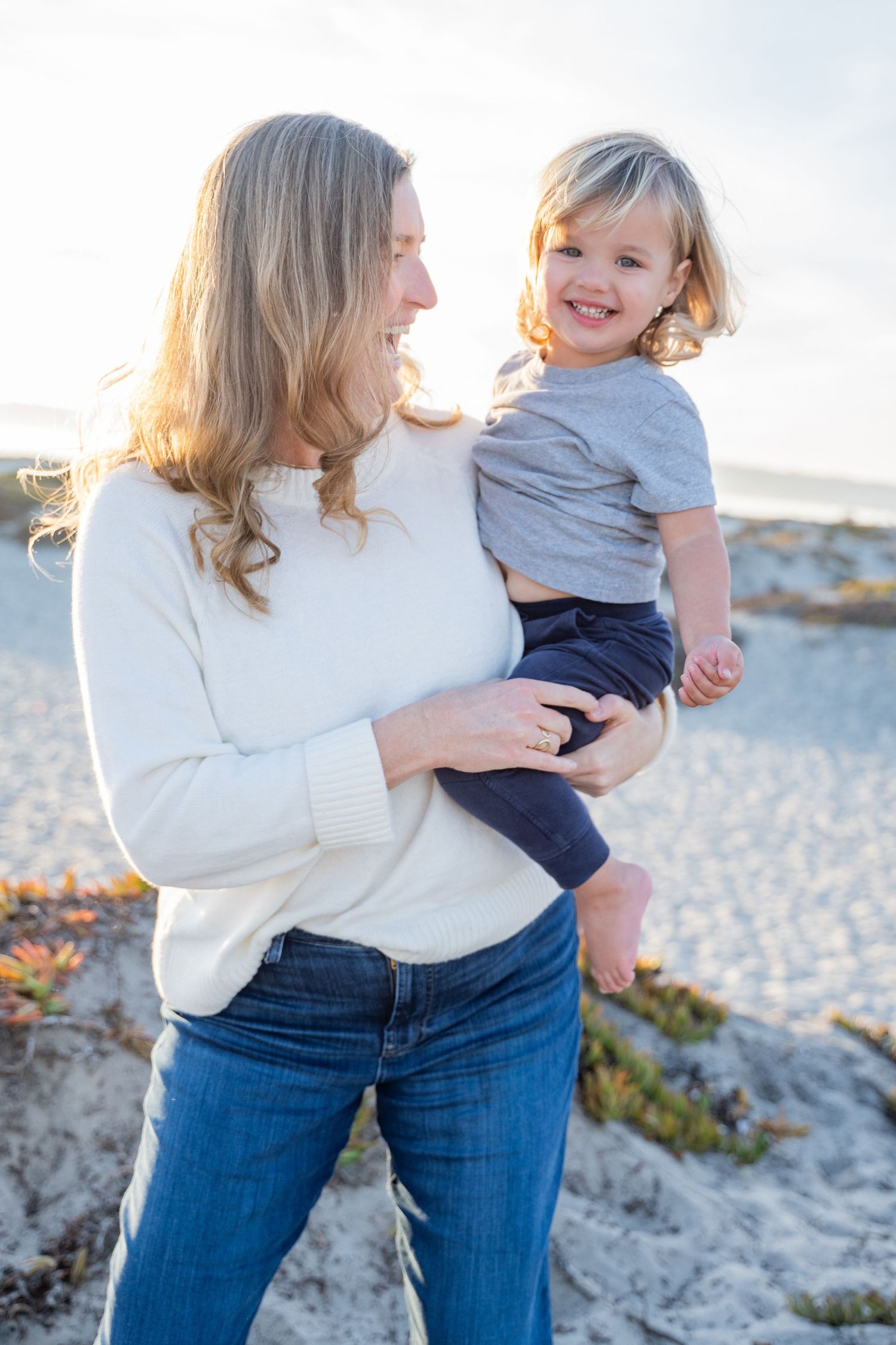 Candid photo of mom laughing with her young child on the sand at golden hour – Coronado family beach session
