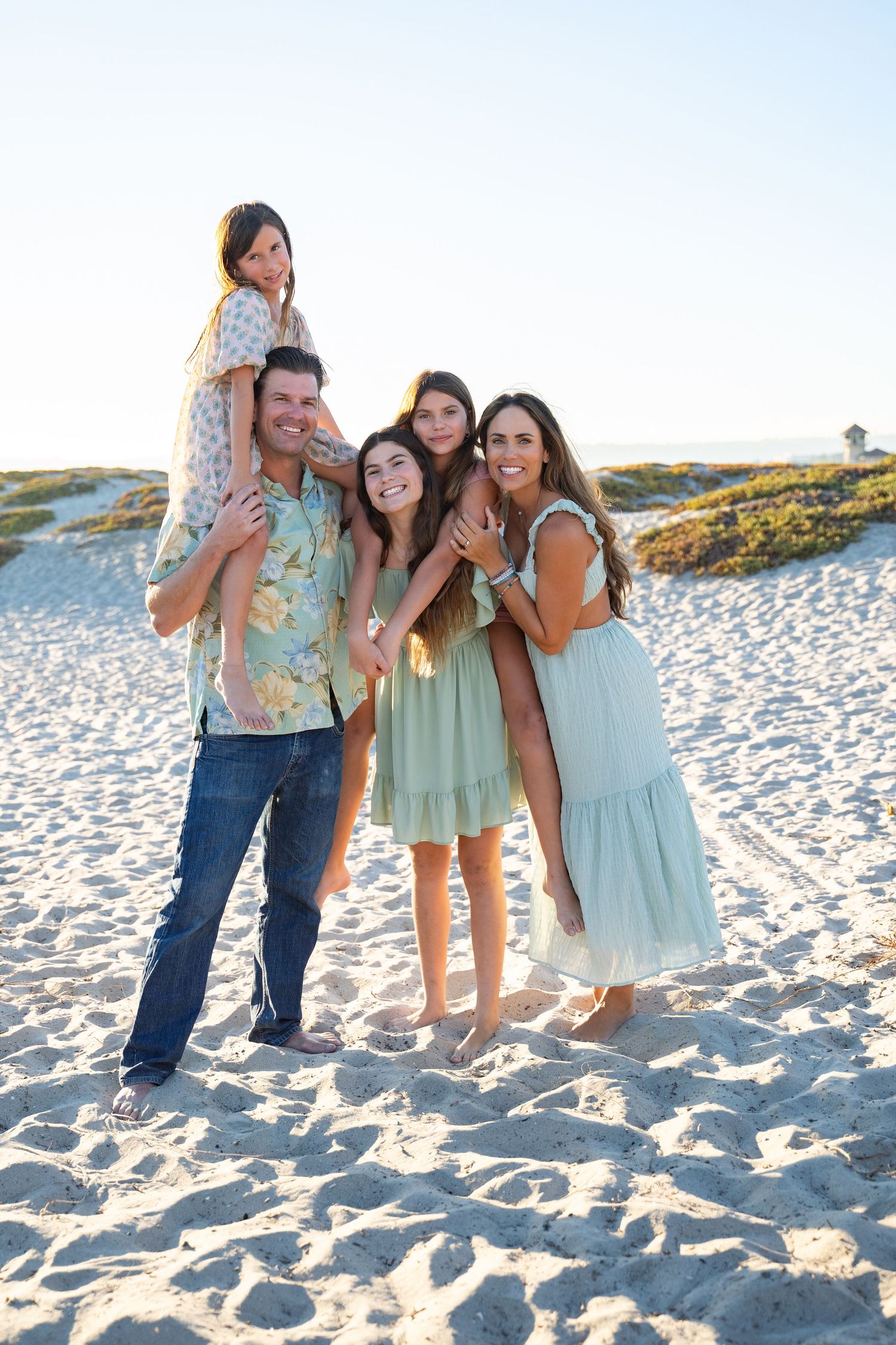 Playful family moment with parents and three girls laughing together in the sand – lifestyle session in Coronado