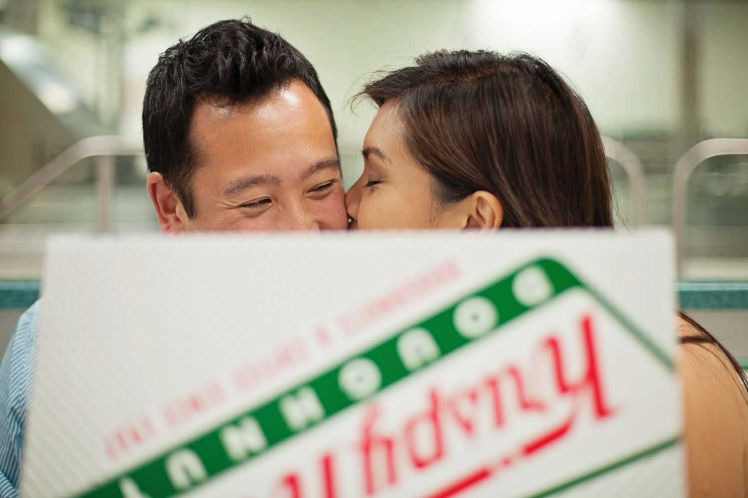 Playful couple sneaking a kiss behind a Krispy Kreme box – candid lifestyle photo with sweet details