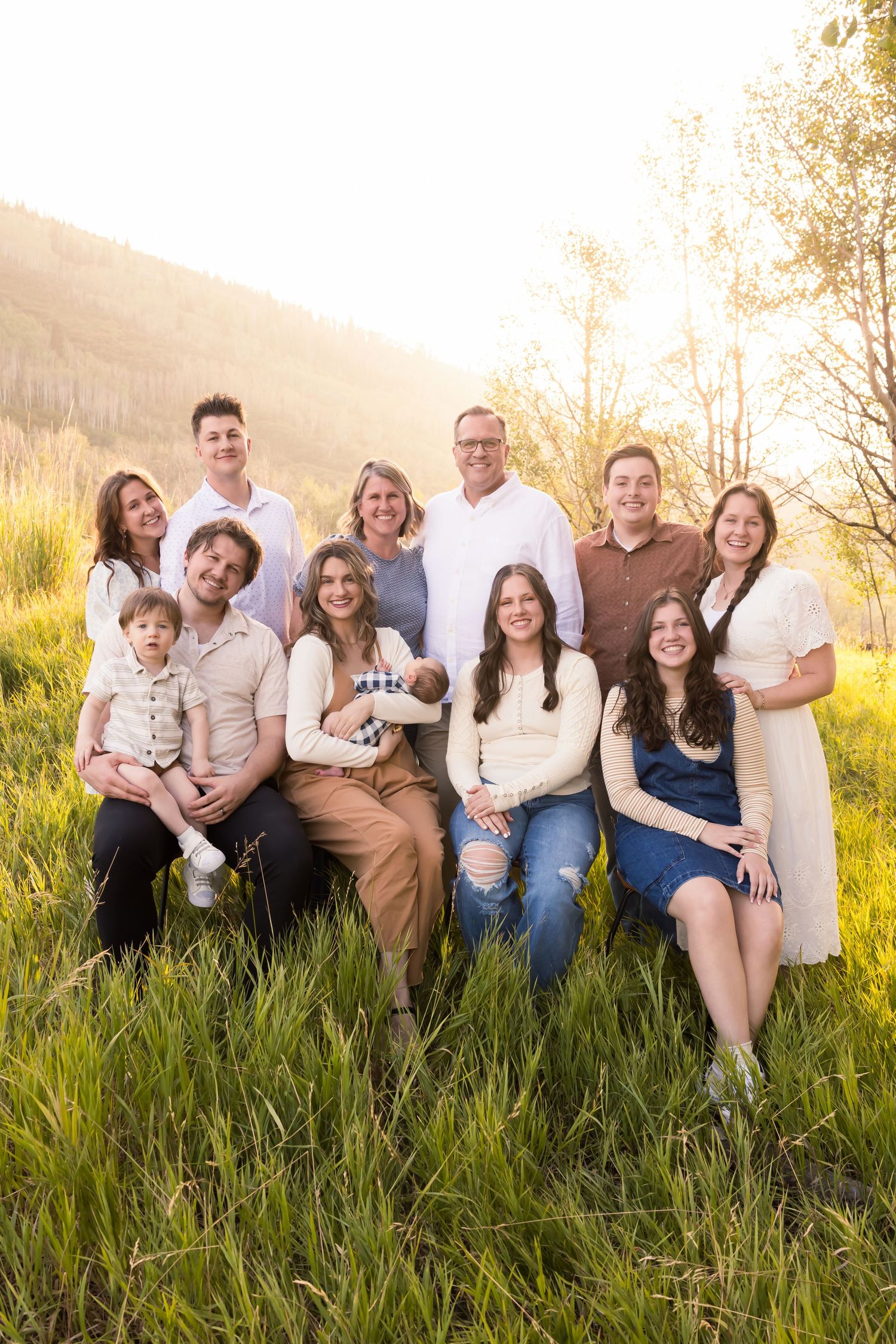 A group sits together in a field of tall grass at golden hour during a casual outdoor photo session.