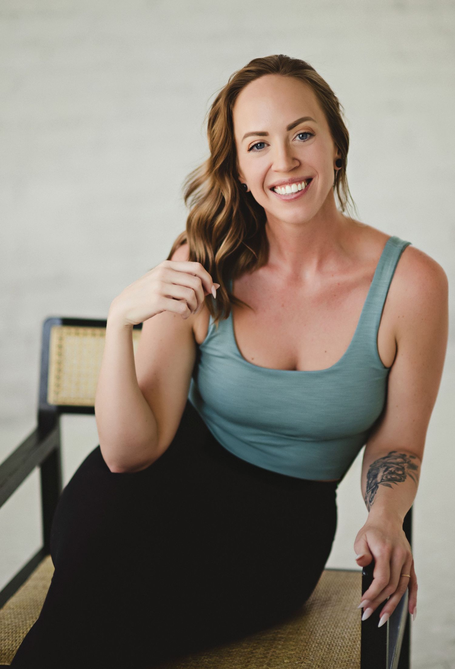 Portrait of woman in teal tank top sitting casually on chair.