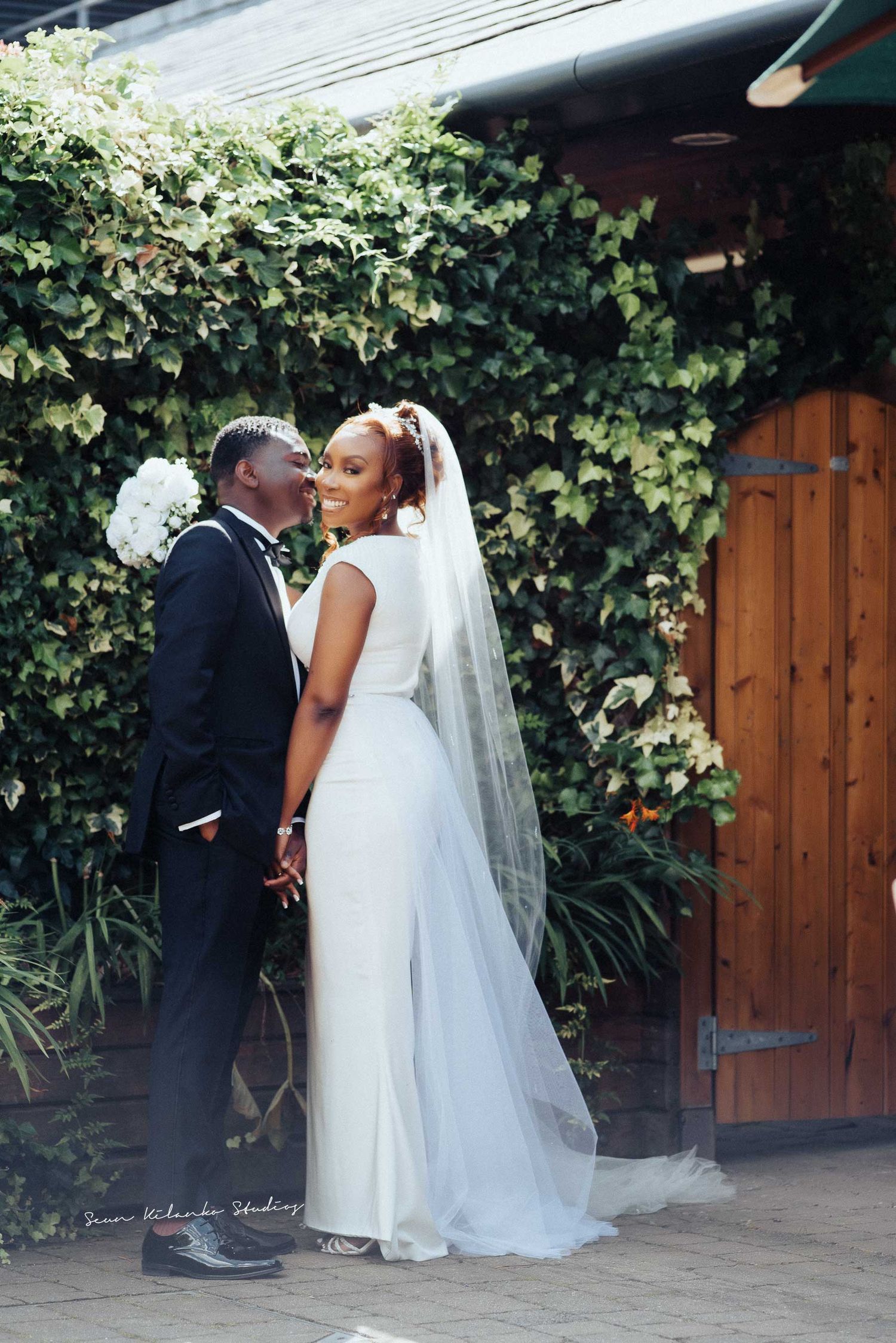 Romantic couple sharing an intimate moment against an ivy-covered wall on their wedding day.