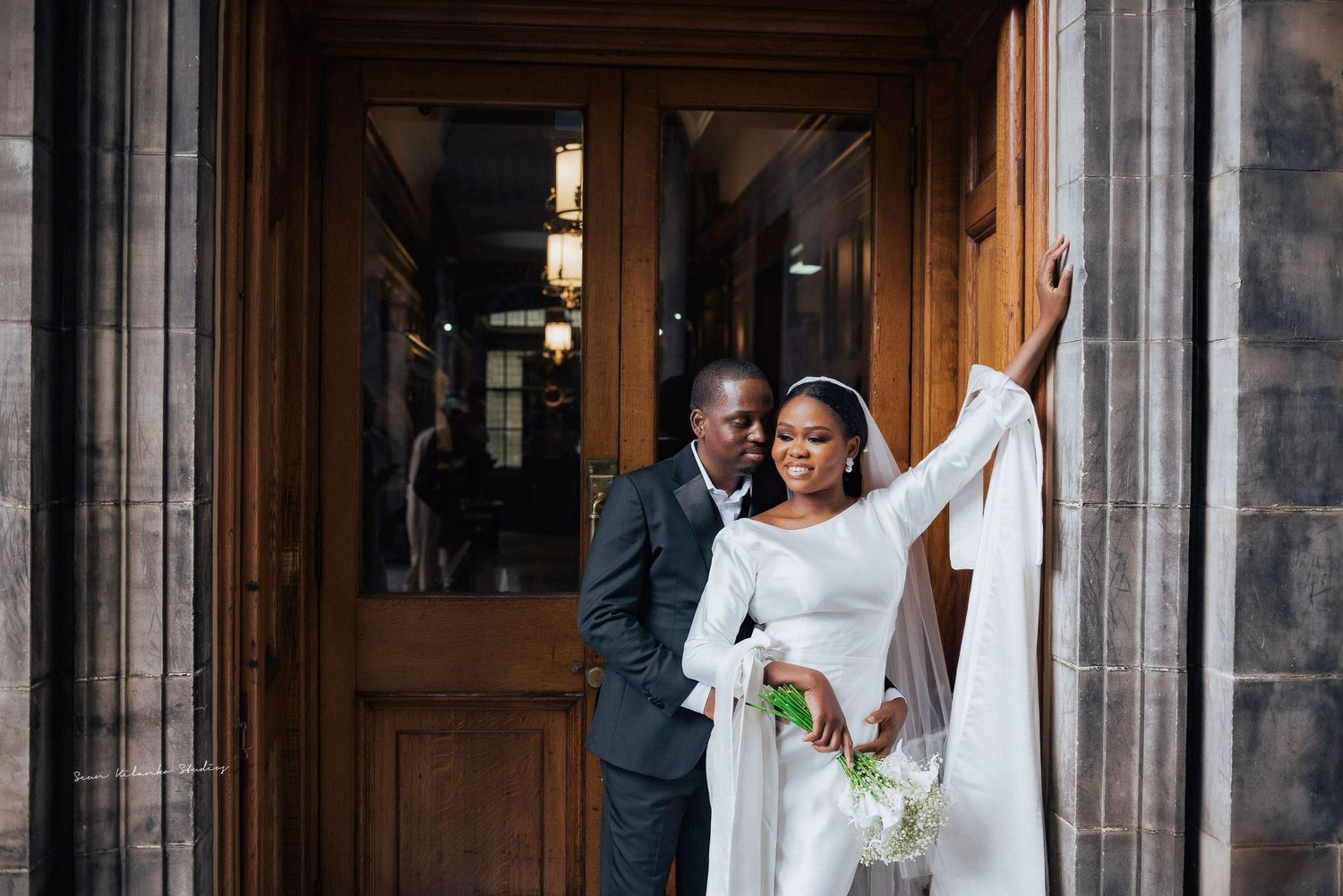 Wedding couple shares a joyful moment by wooden church doors.