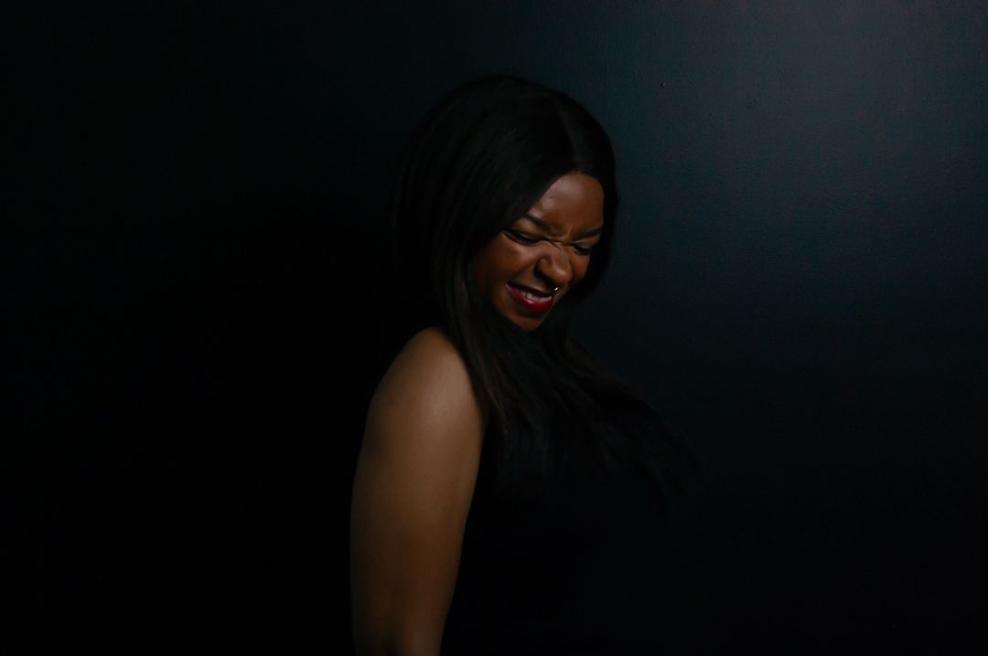 Dark artistic portrait showing a joyful expression against a black backdrop.
