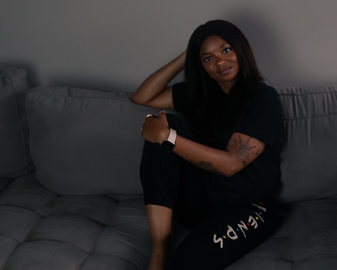 Person wearing all black lounges casually on a grey couch in dim lighting.