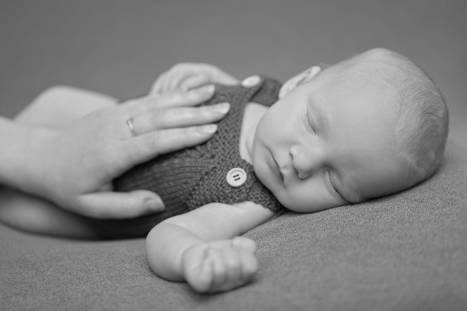Black and white image of sleeping baby wearing knit outfit with hand gently touching.
