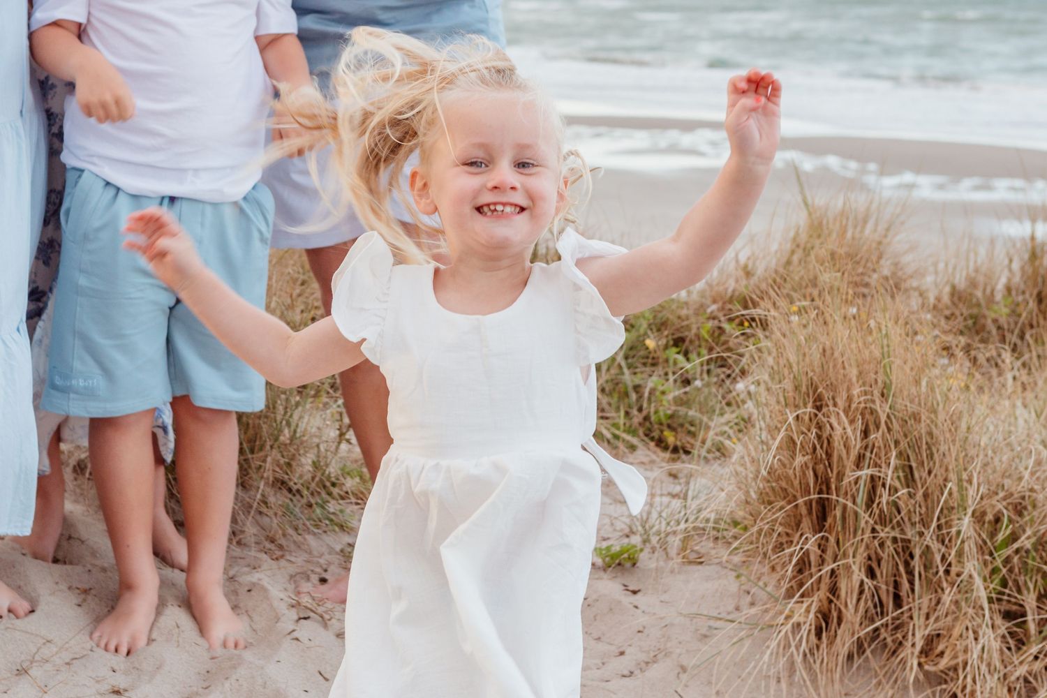 A carefree moment of dancing and twirling in a white dress on a sandy beach path.
