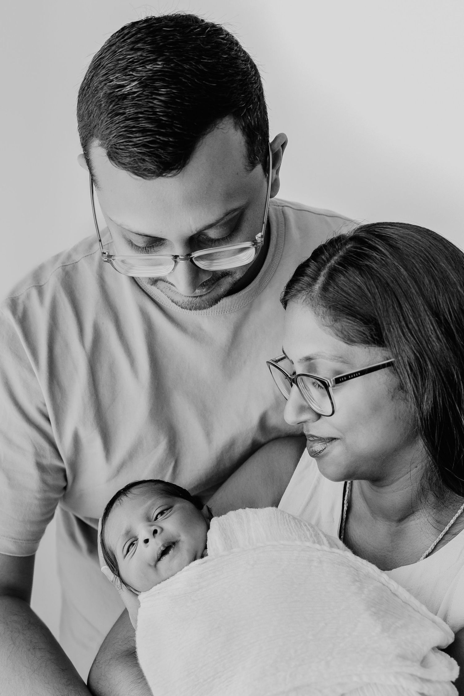 Black and white portrait of parents gazing lovingly at their newborn.