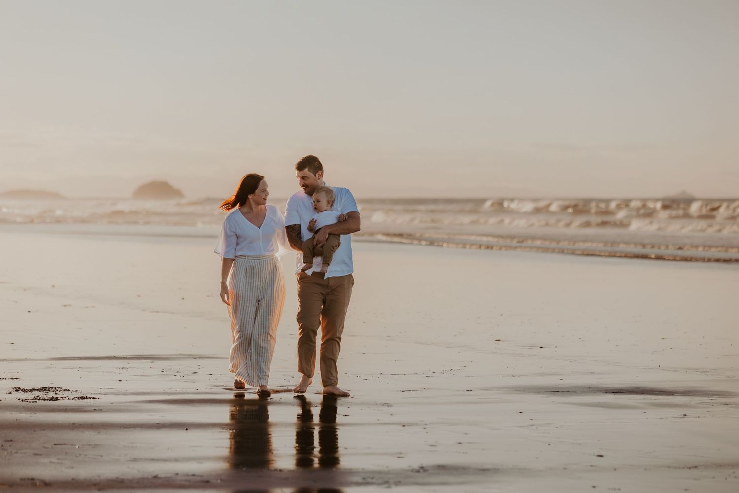 Couple walking together on misty beach while holding their baby.