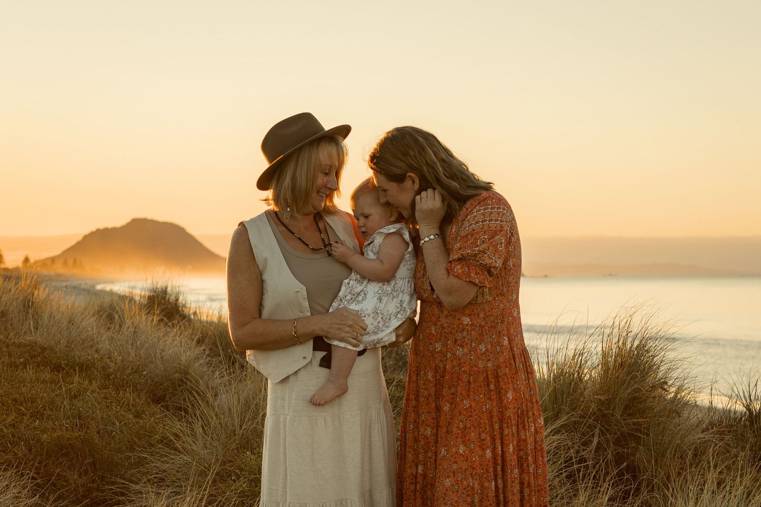 Three figures share an intimate moment against a golden sunset overlooking the ocean.