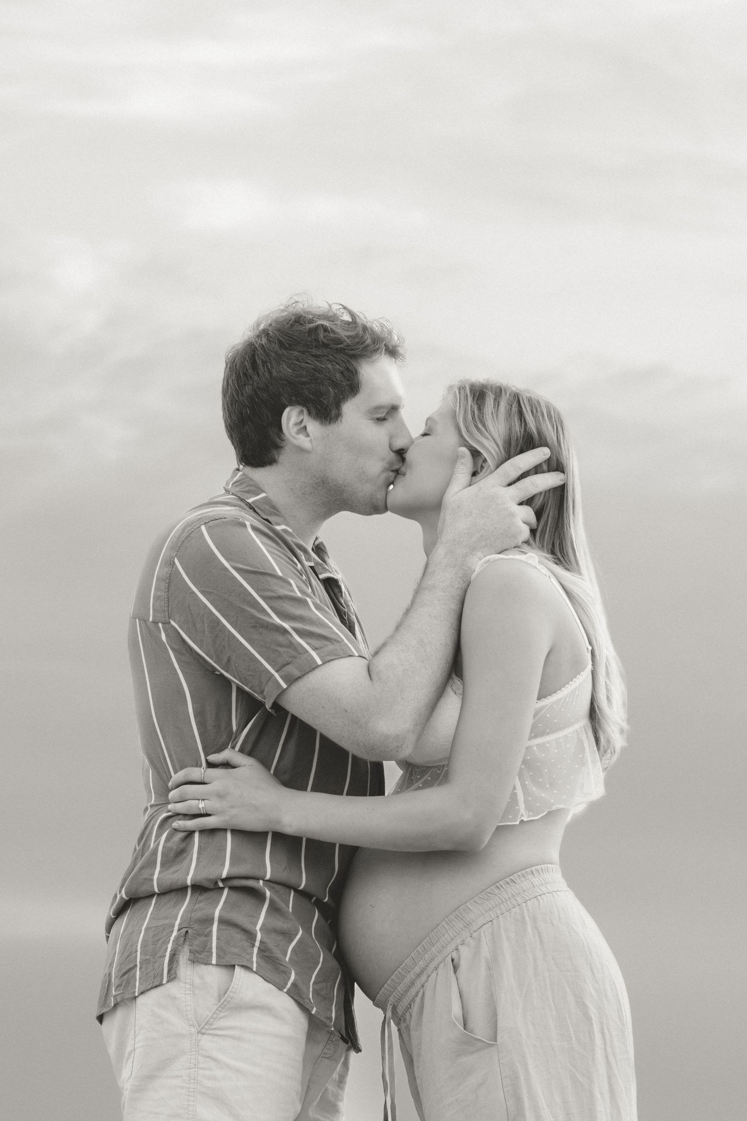 Romantic couple sharing an intimate moment against cloudy sky in monochrome.