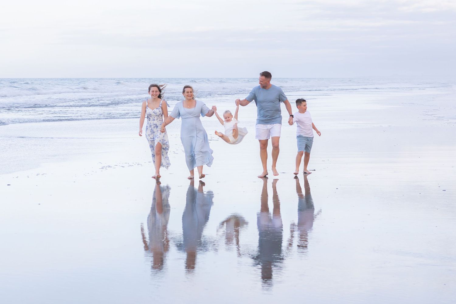 A family holding hands while walking along a reflective beach shoreline at dusk.