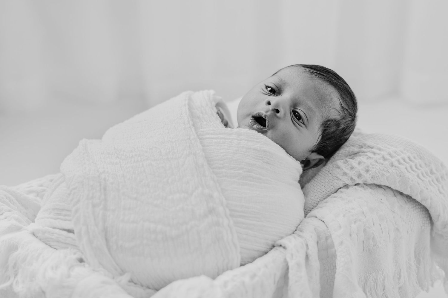 Side view of sleeping baby in white swaddle against light background.