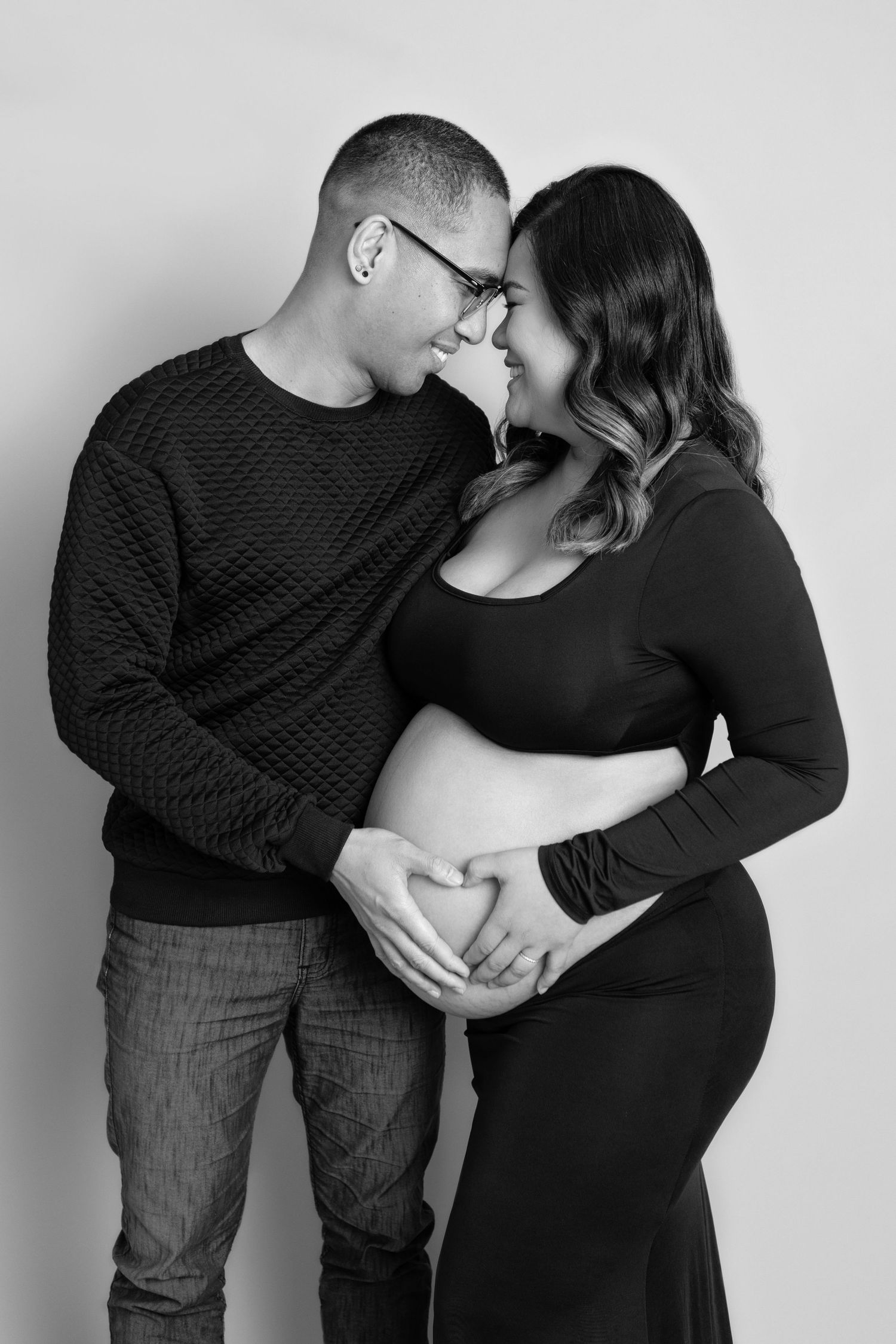 Black and white portrait of expecting couple in matching dark outfits.