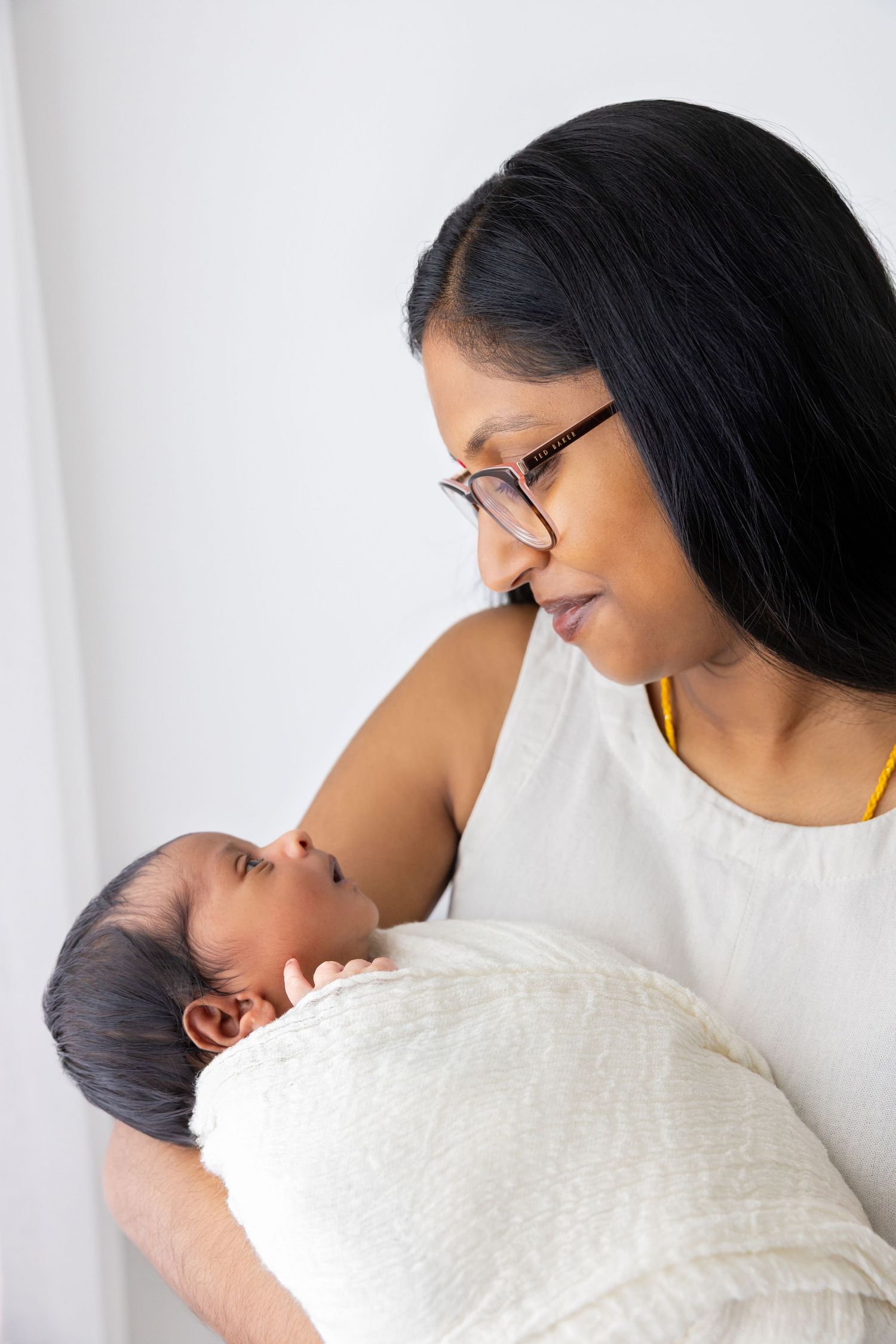Loving parent holding newborn baby swaddled in soft white blanket.