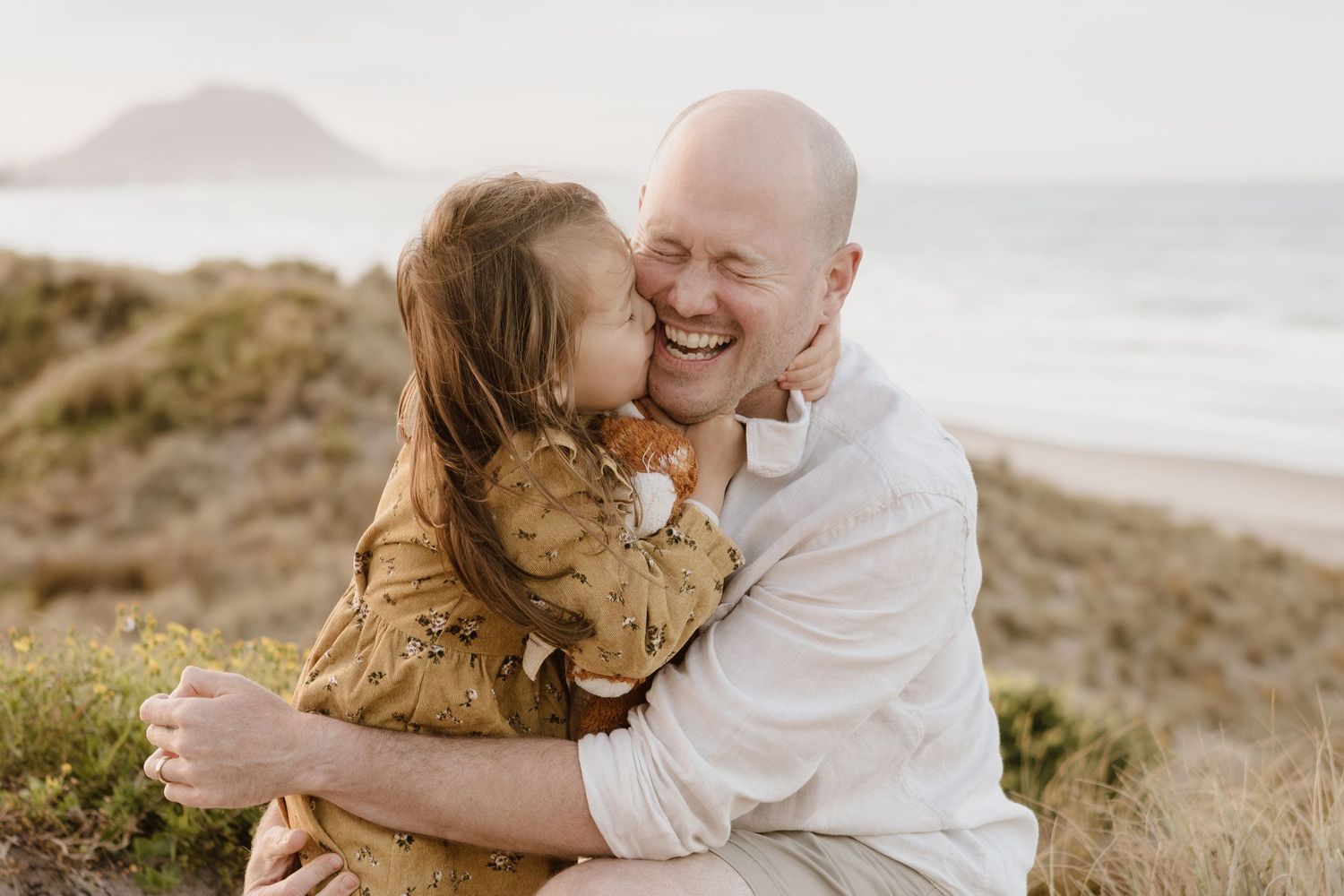 Intimate embrace shared between two people on grassy coastal hillside.