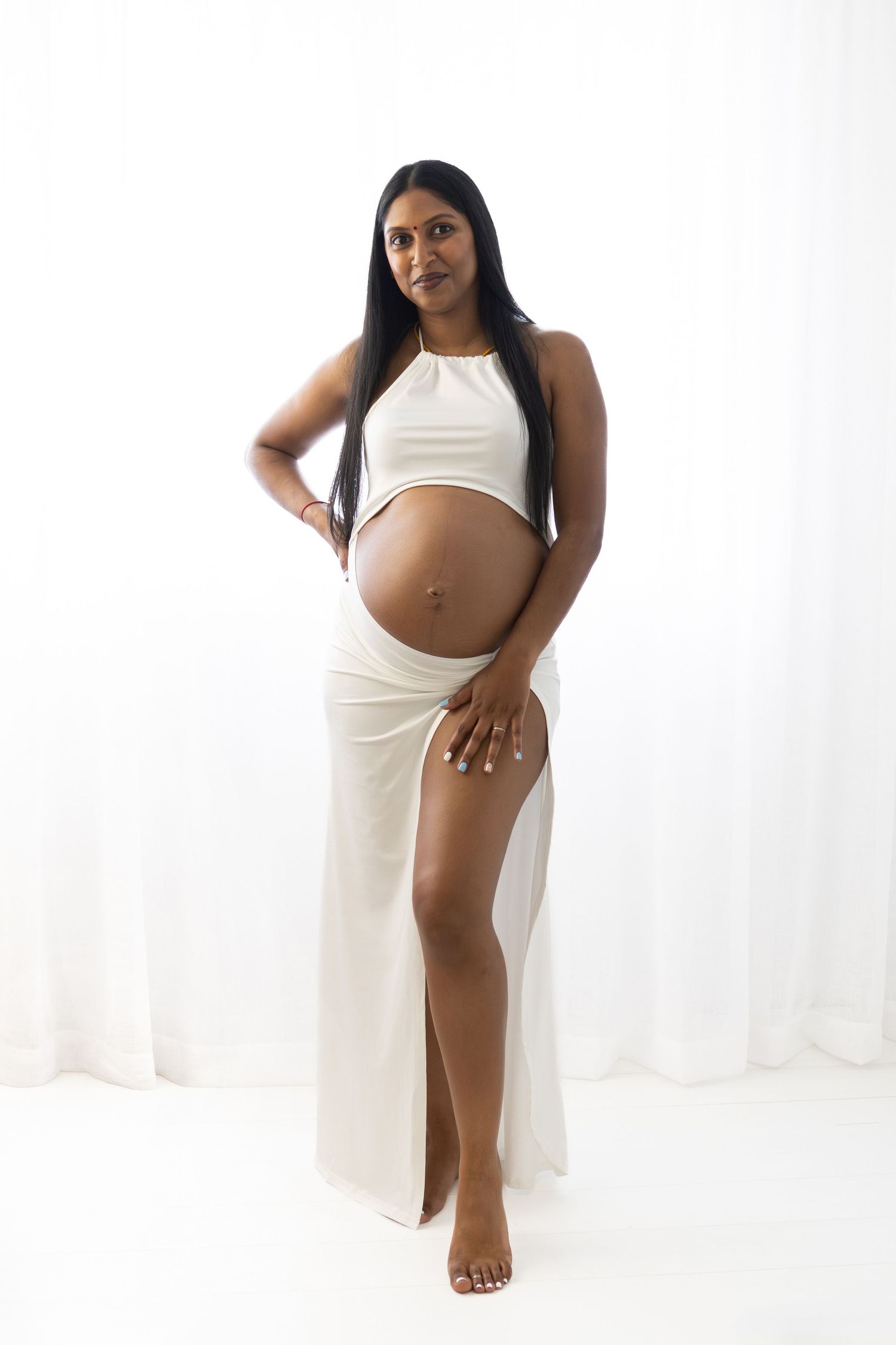 Creative maternity photoshoot in cream-colored dress showing pregnancy silhouette.