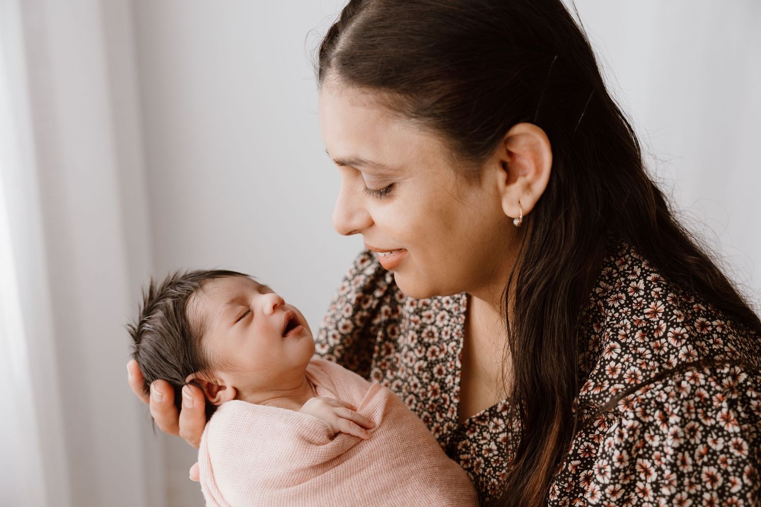 A gentle moment between parent and newborn baby against a white background.