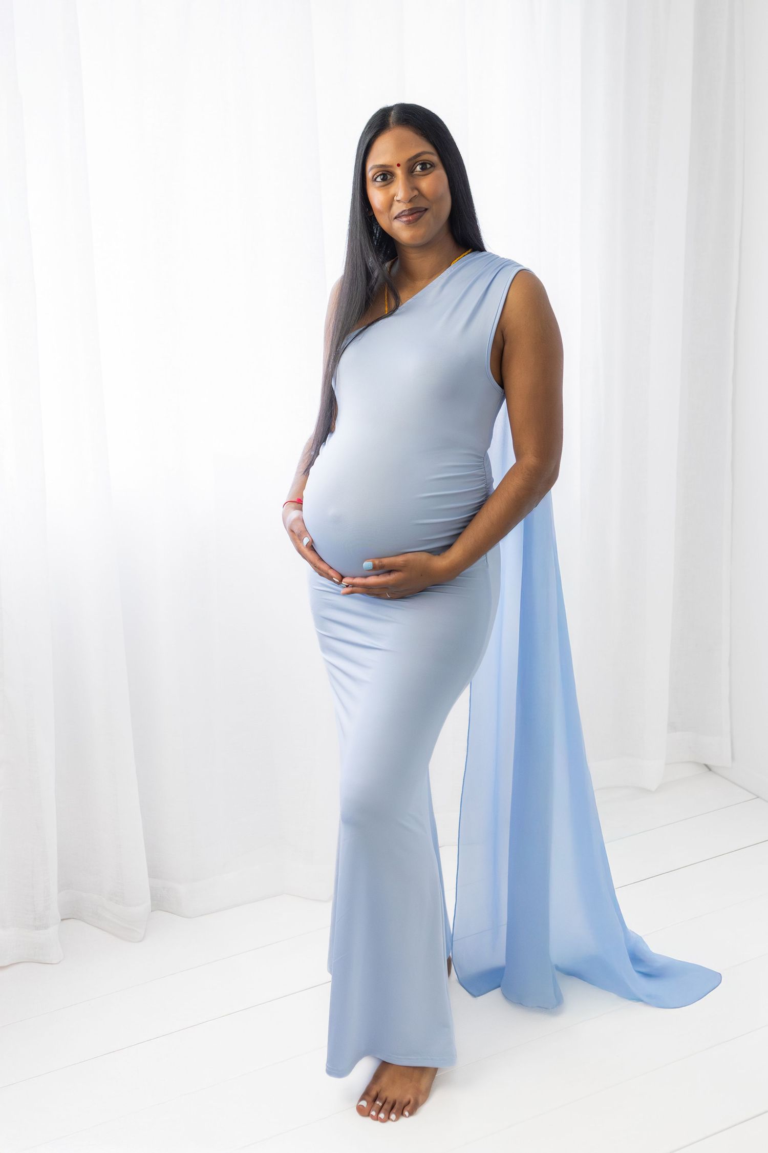 Artistic maternity photos in powder blue dress with flowing fabric against white background.