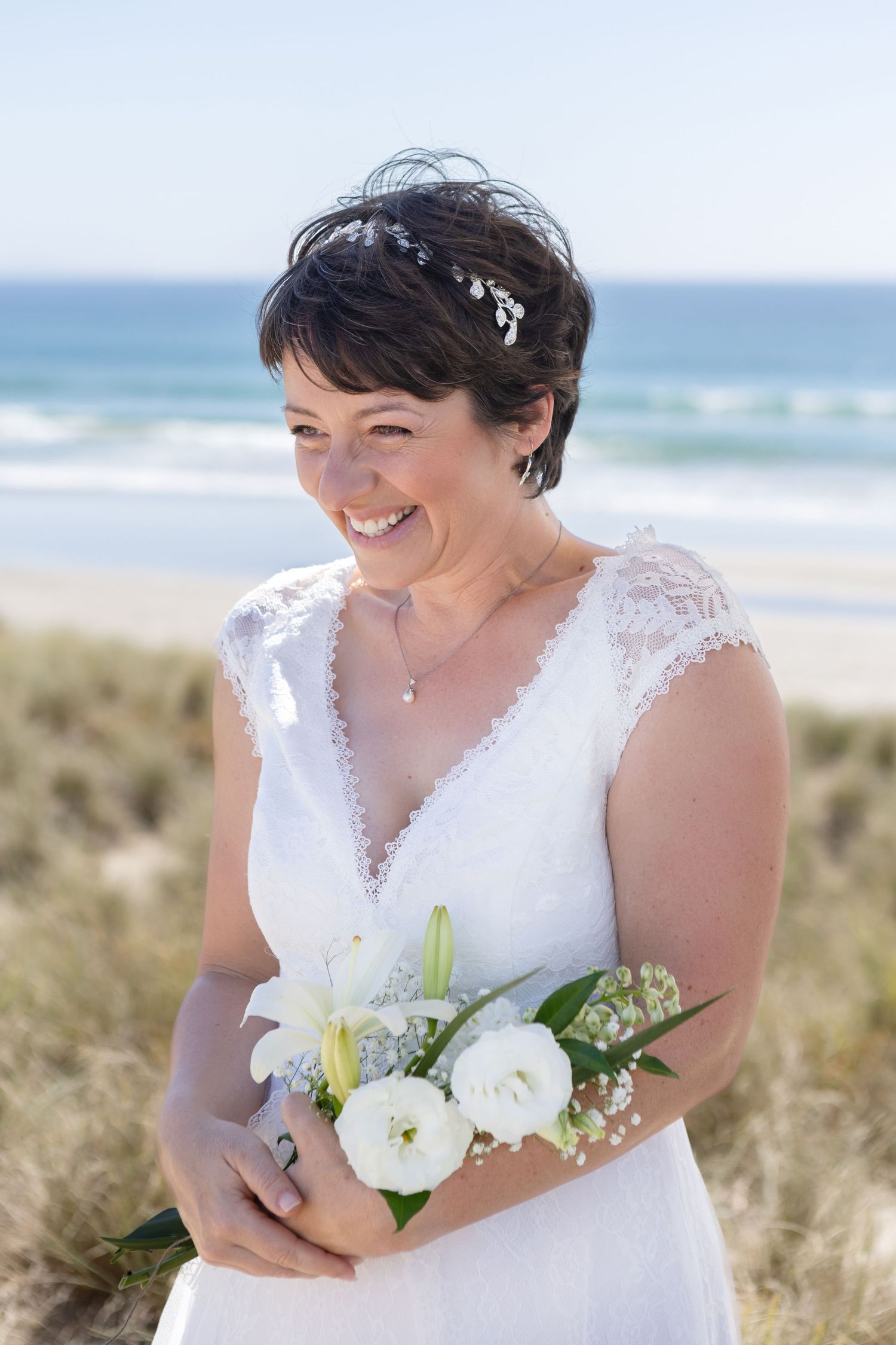 Bridal portraits at a beach with white bouquet and lace dress details.