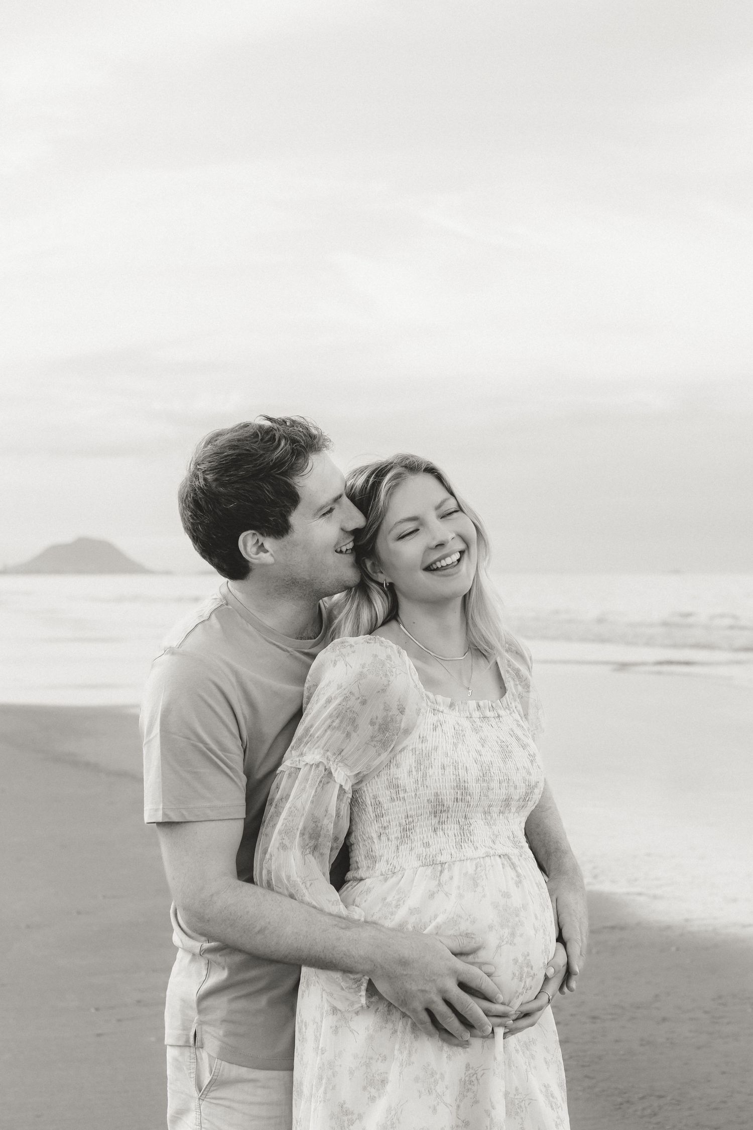 A black and white maternity portrait of a couple sharing an intimate moment on the beach.